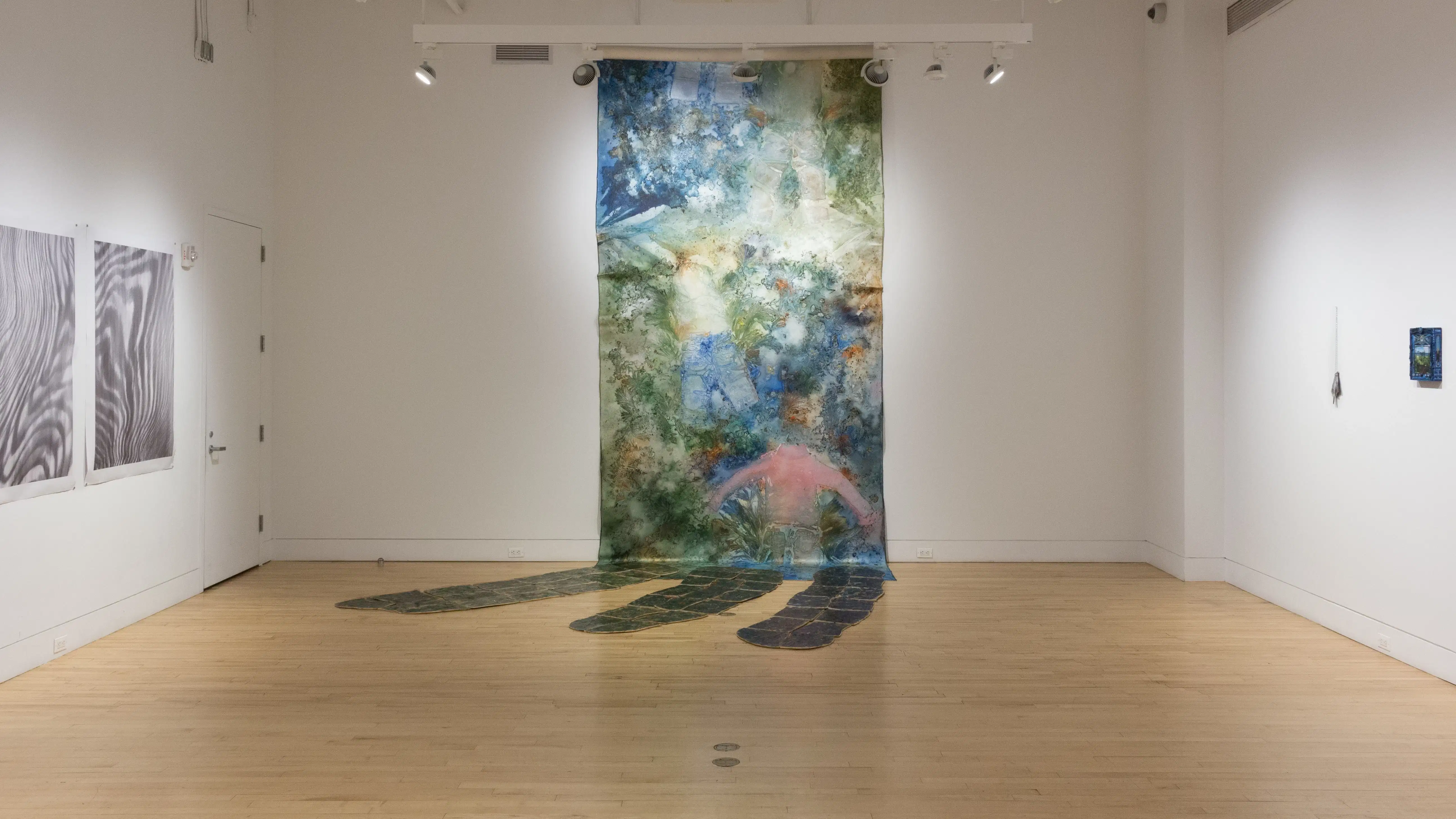 A view of the back wall in the SVA Flatiron Gallery, highlights a wall sized painting and installation piece that expands out onto the floor. 