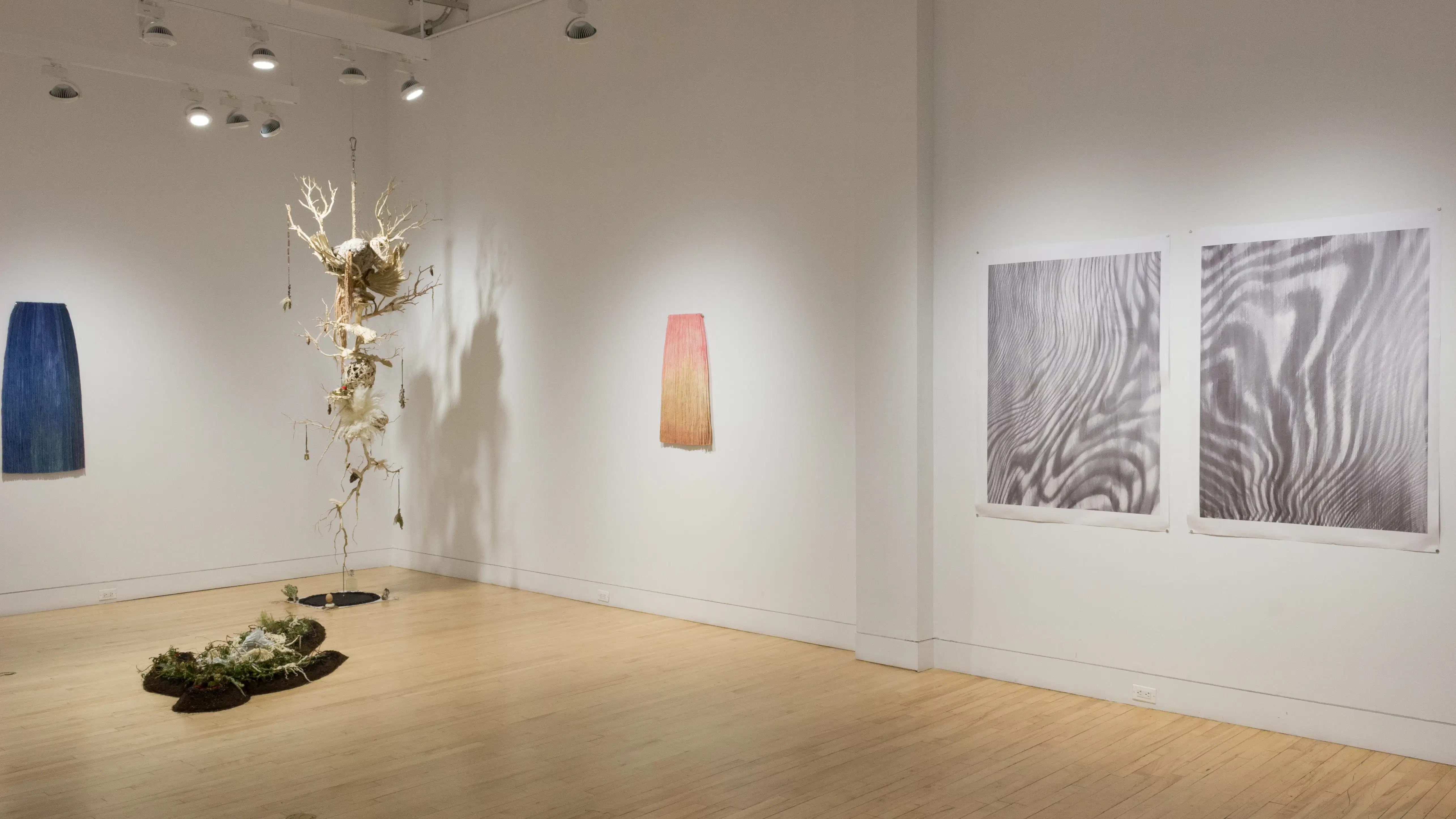 An angled view of the left wall in the SVA Flatiron Gallery, showcasing a large hanging sculpture, installation pieces, and prints. 