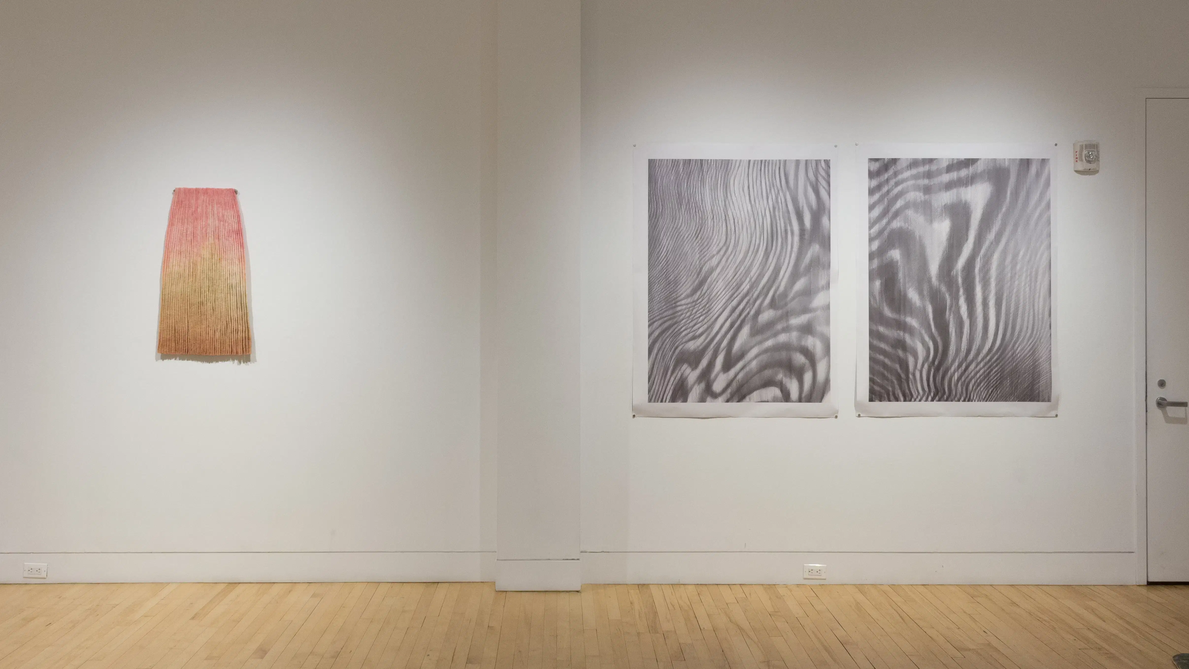 A straight on view of the left wall in the SVA Flatiron Gallery shows a colorful wall sculpture and two prints. 