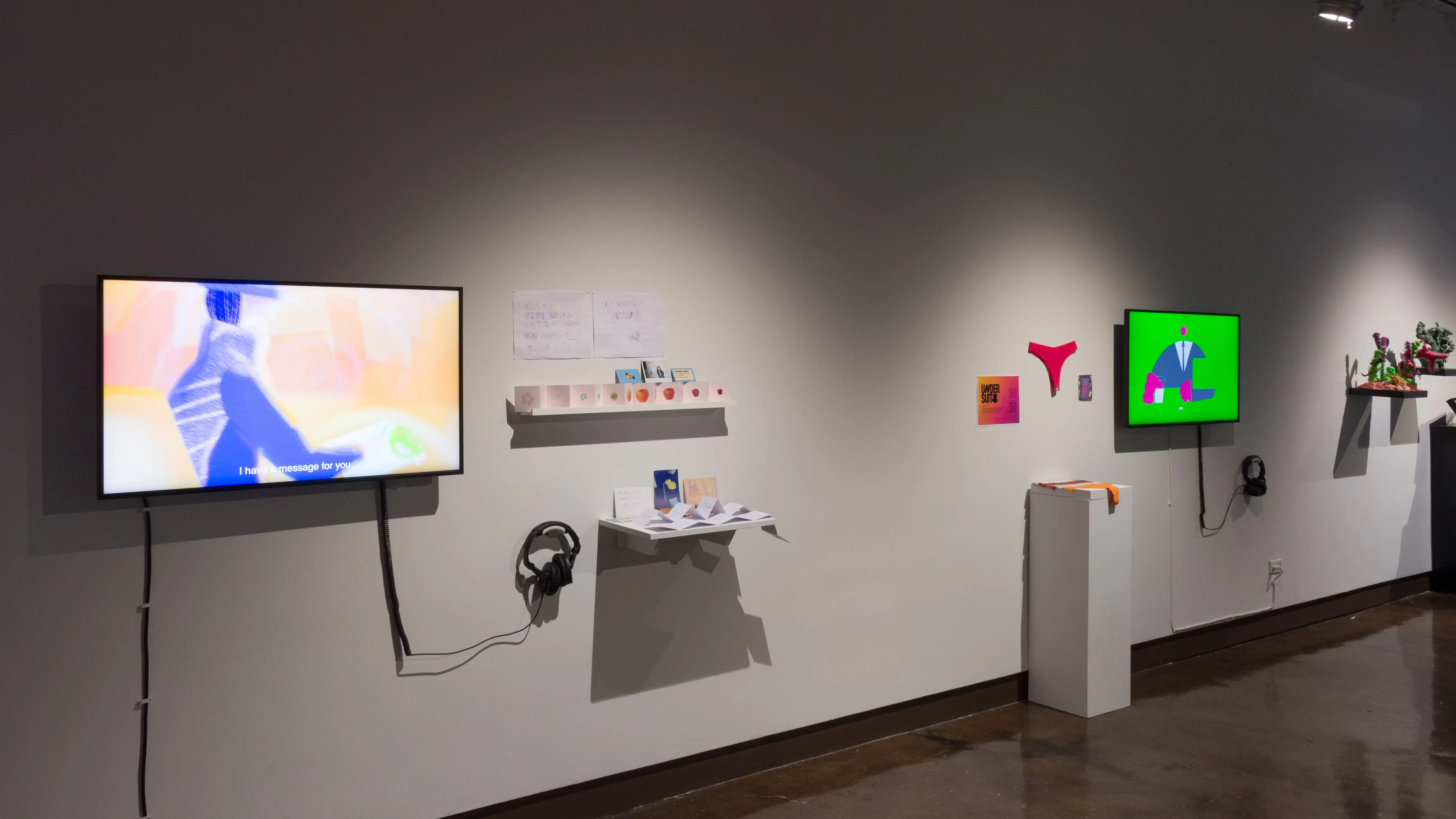 Angled wall with two monitors and several shelves and pedestals visible, receding into the background.