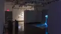 Installation image of a gallery alcove with a large projection of a mushroom to the right, and several pedestals with interactive projections in the foreground to the left.