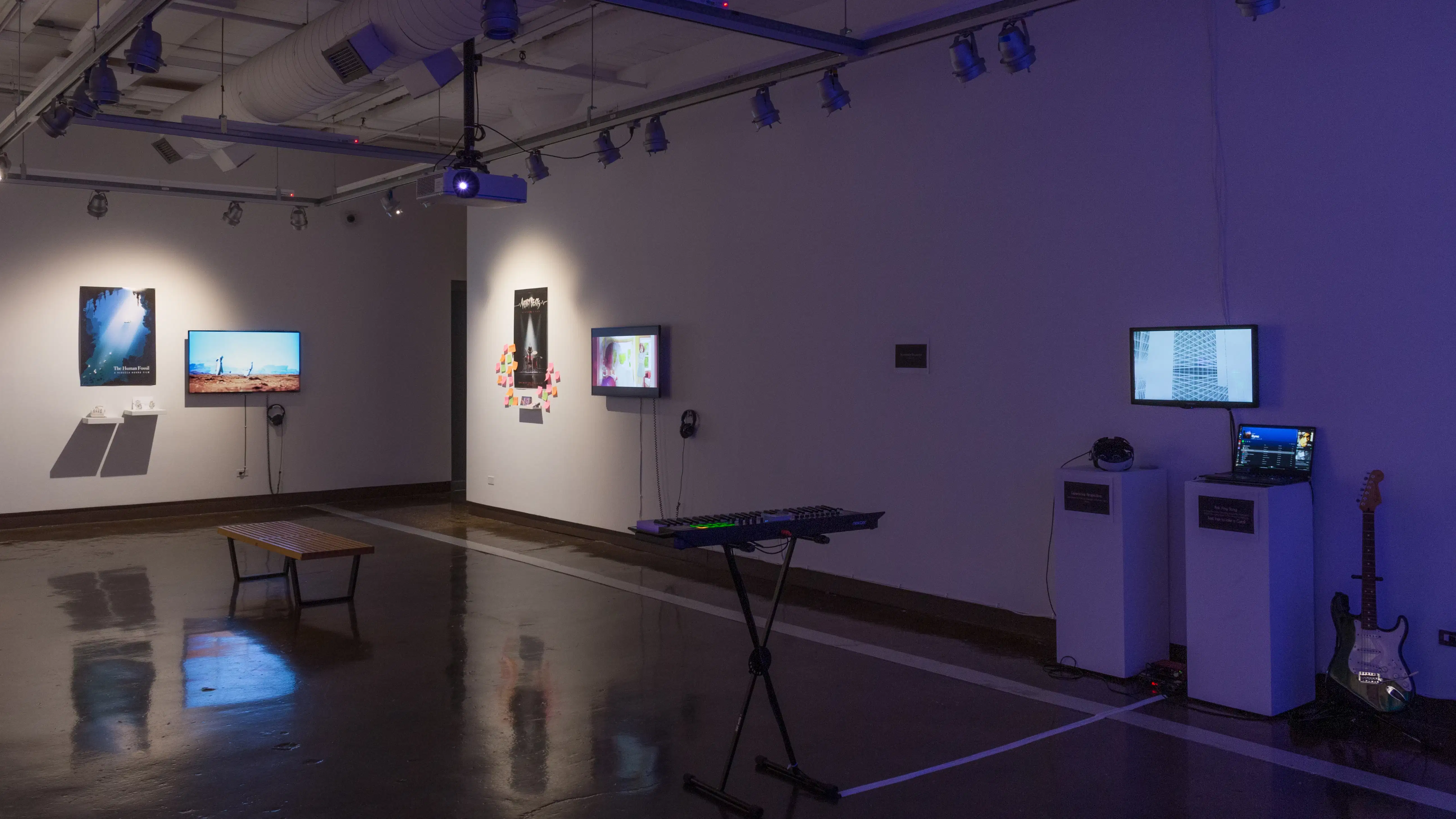 Installation image showing an angled view of a freestanding wall, with musical instruments in the foreground and several monitors and installations in the background.