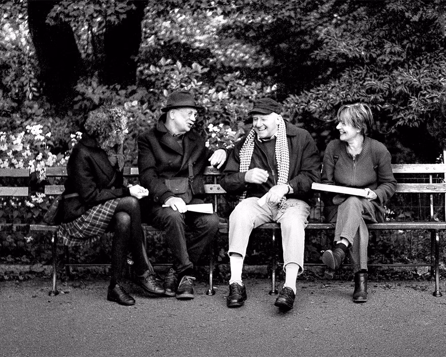 Four friends are sitting shoulder to shoulder in the park talking.