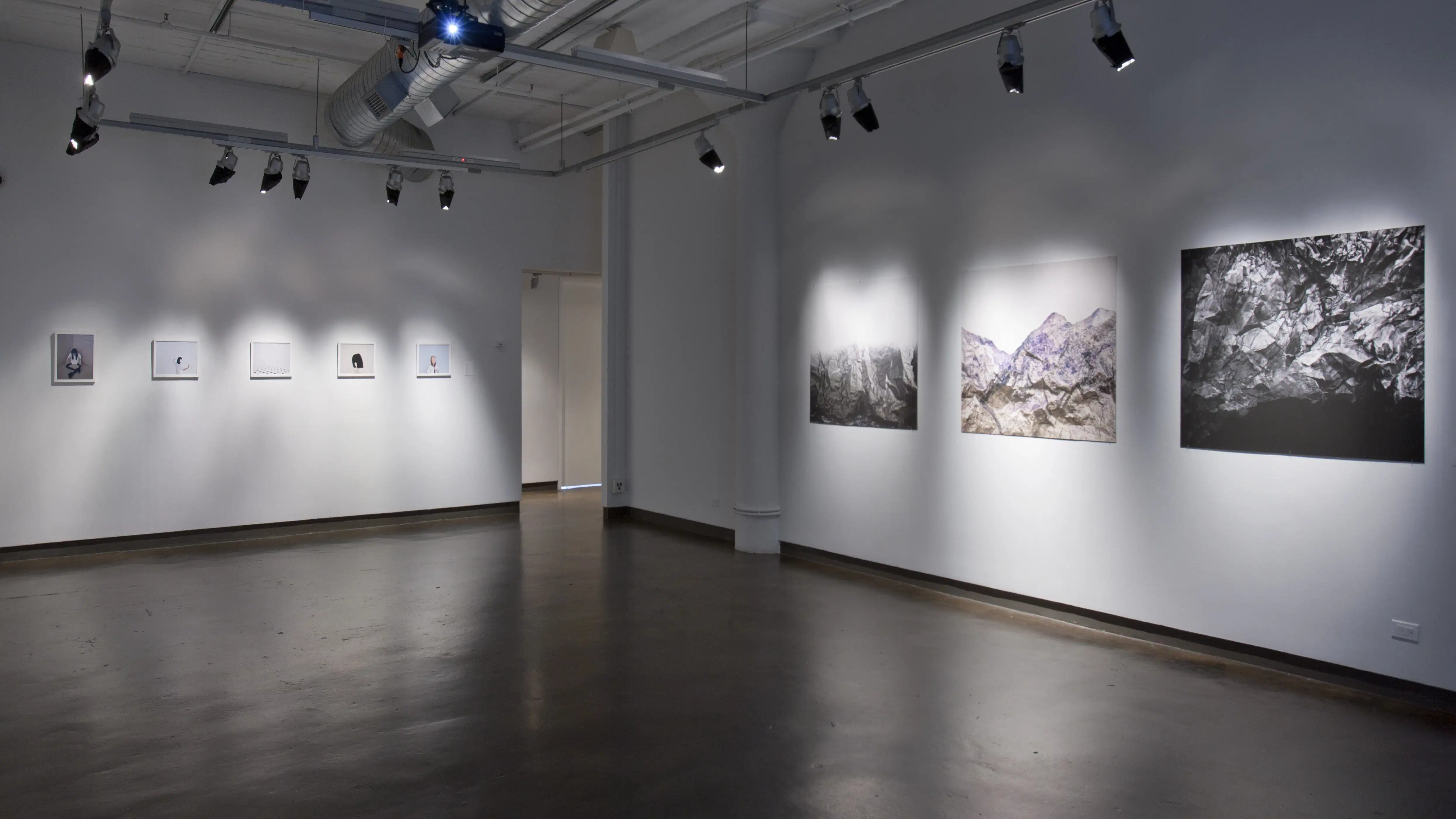 An art gallery displaying black and white pictures of mountains and trees and smaller black and white pictures that are too far away to see what the pictures are.