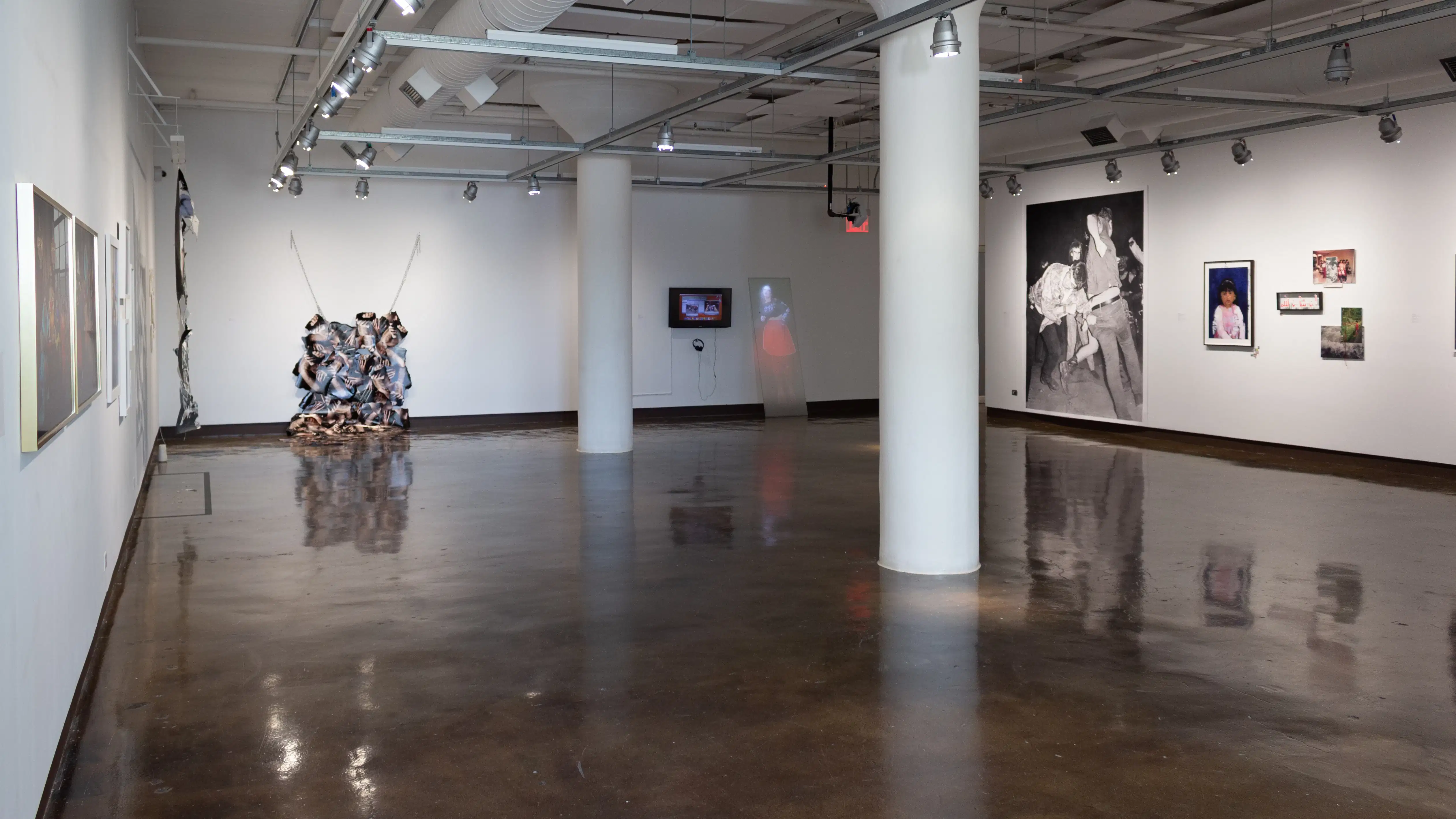 Installation view featuring photographs and photo installations on three walls, with two large white columns in the middle.