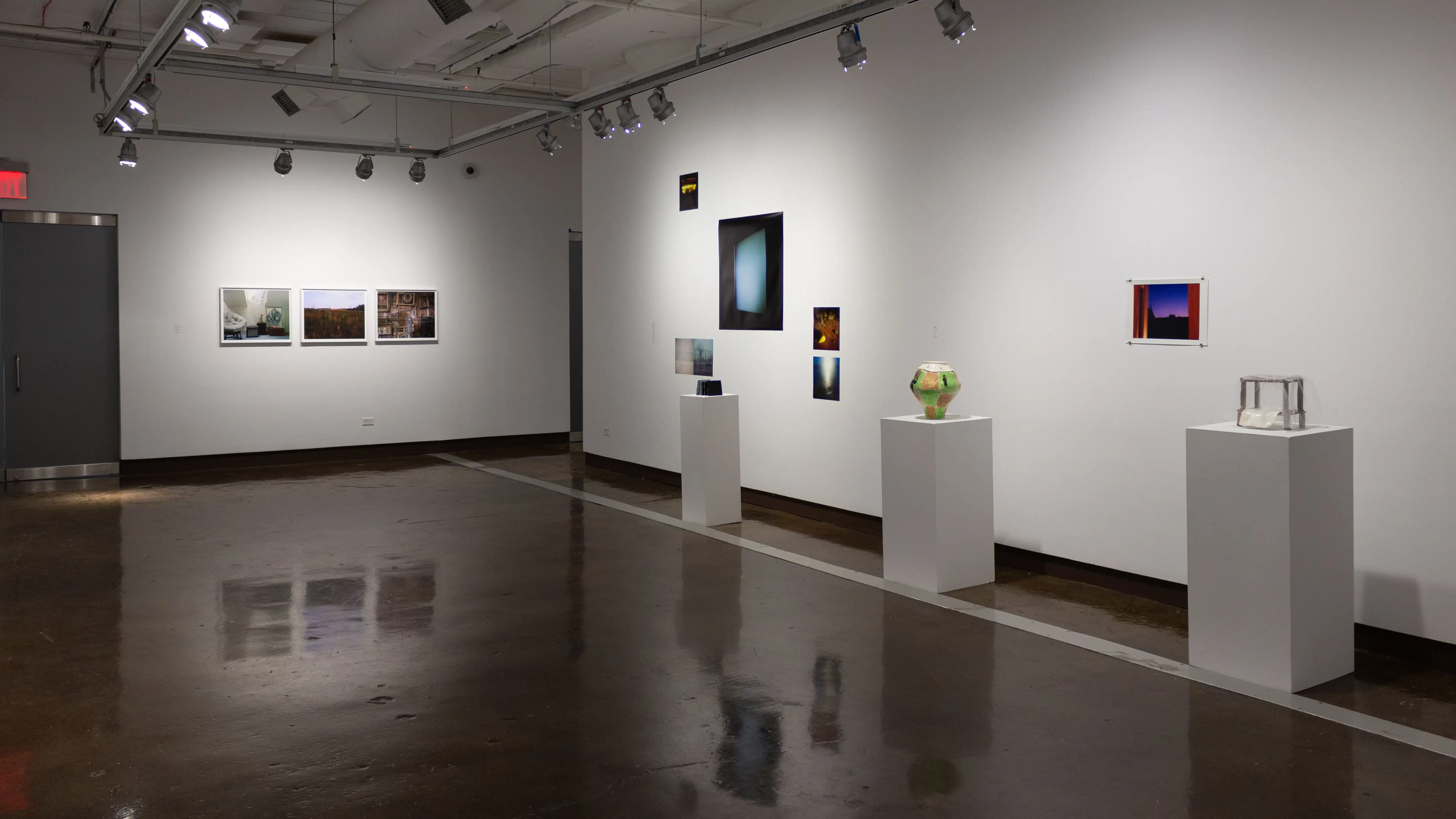 Installation image showing 3 color photographs on the far back wall, three pedestals with ceramics and unframed photo installations behind.