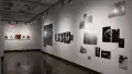 Installation image showing installations of black and white and color photographs on a long wall on the right, and 5 framed color photos on a far back wall.