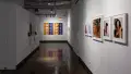 Installation image of a hallway with a monitor on the left, a large color grid on the wall in the back and 5 color photographs on the right wall.