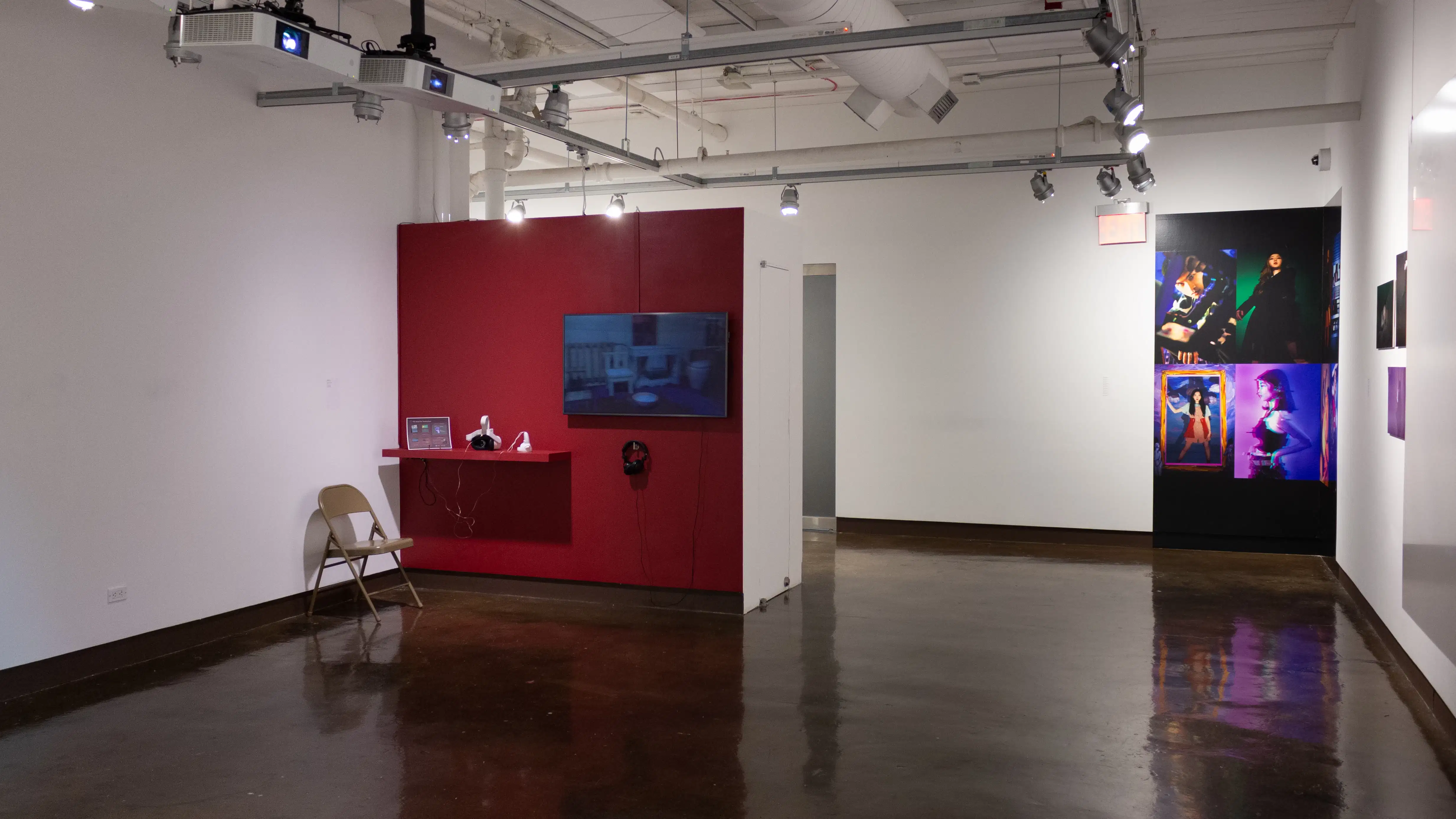 Installation image showing a red wall with a shelf, monitor and chair on the left, and a colorful installation spanning two walls in the corner on the right.