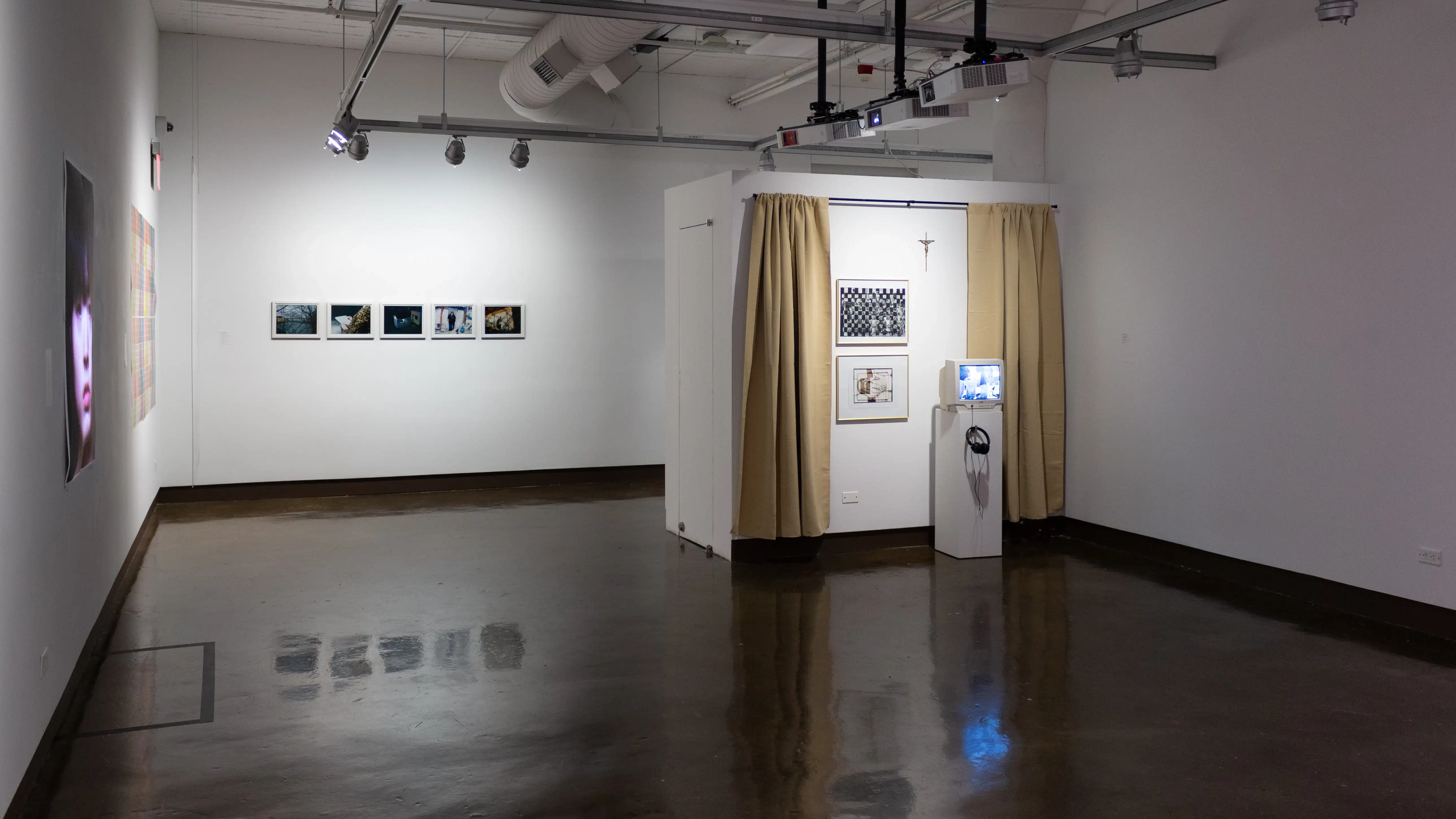Installation image with a tan curtain and a monitor on a pedestal on the right, a portrait on the left, and 5 framed photos on the back wall.