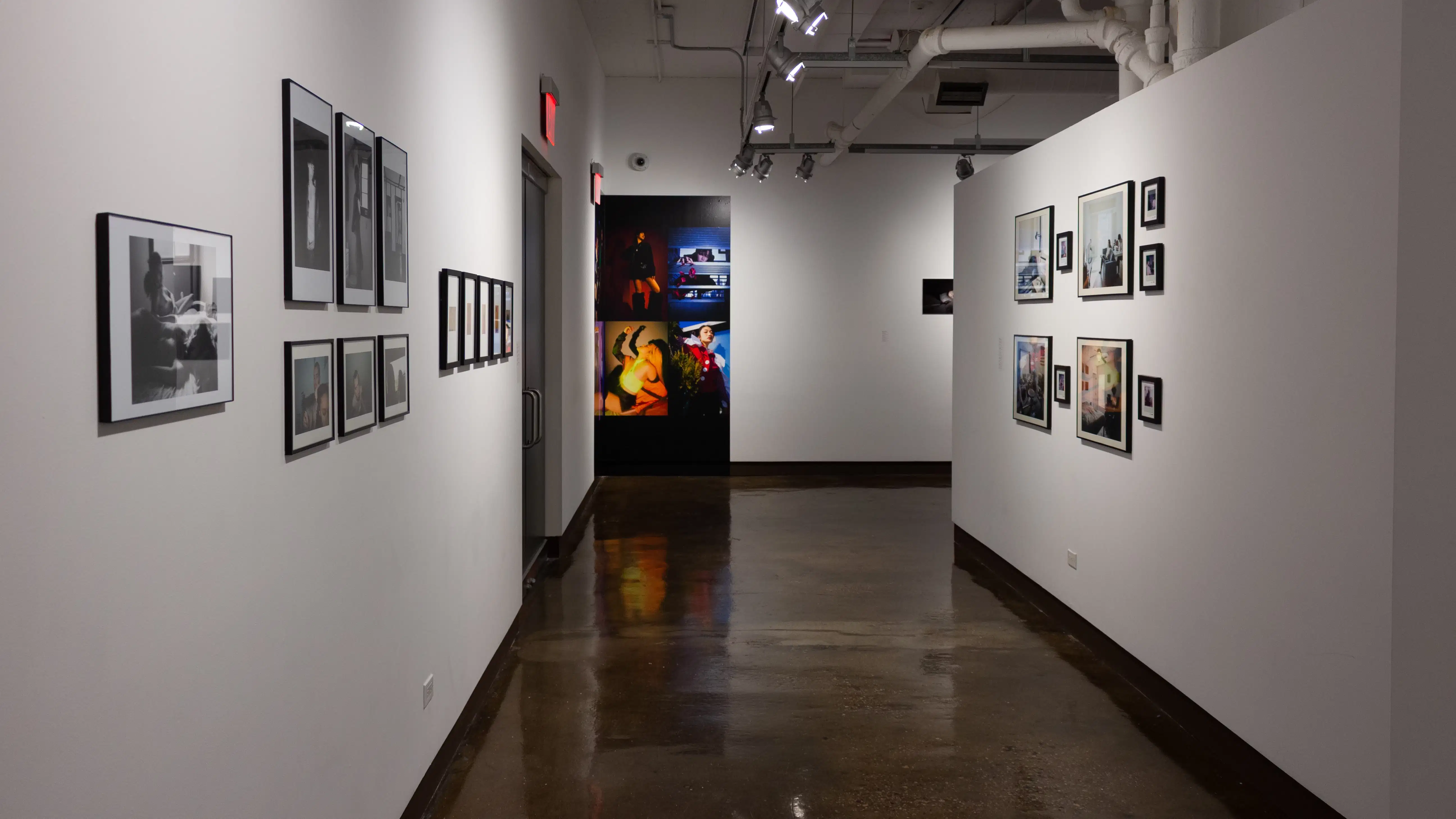 Installation image showing a hallway with 12 framed photos down the left wall, a color installation on the back wall and 9 color framed photos on the right wall.