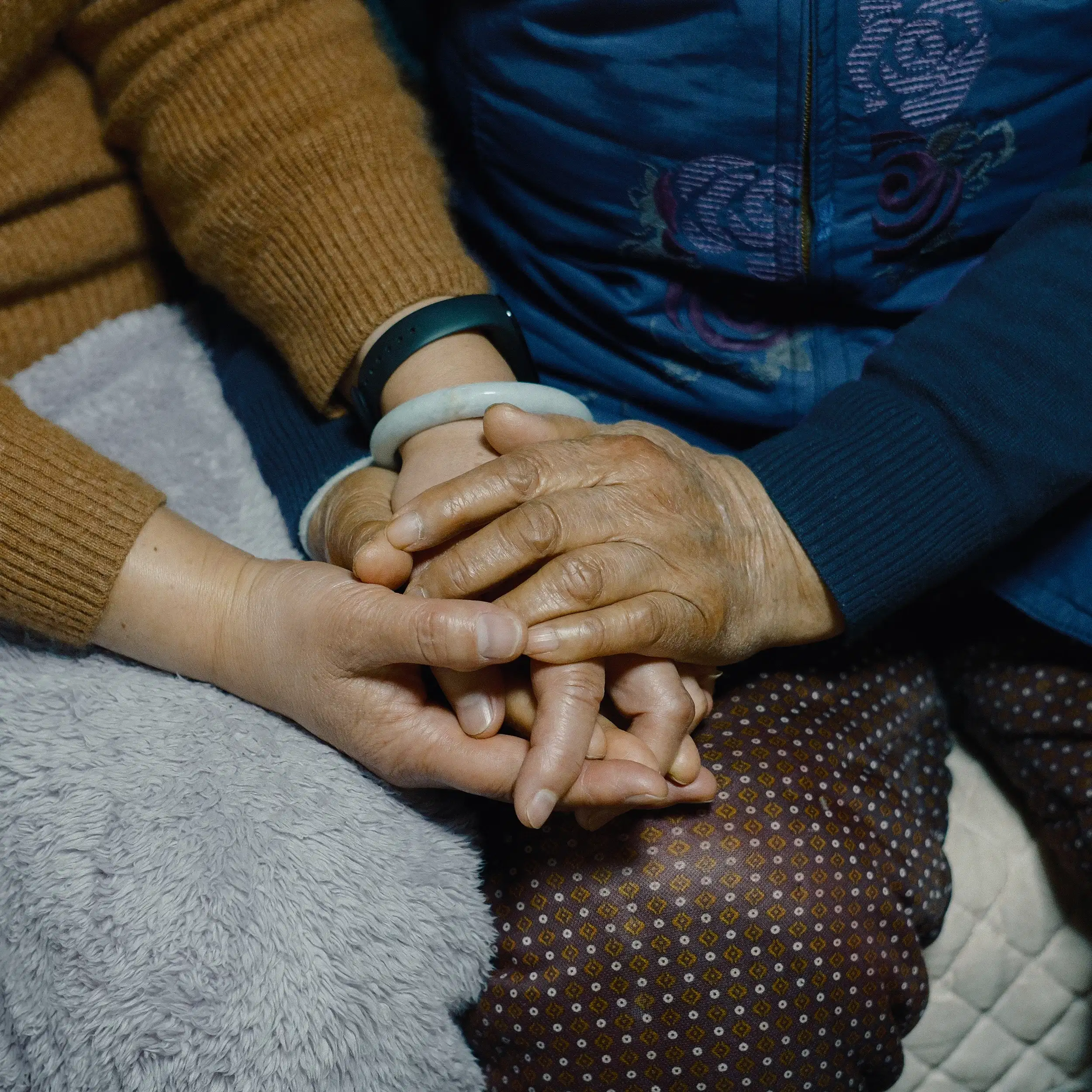 A close-up of a young person's hand holding an elderly person's wrinkled hand, conveying a sense of care and generational connection.