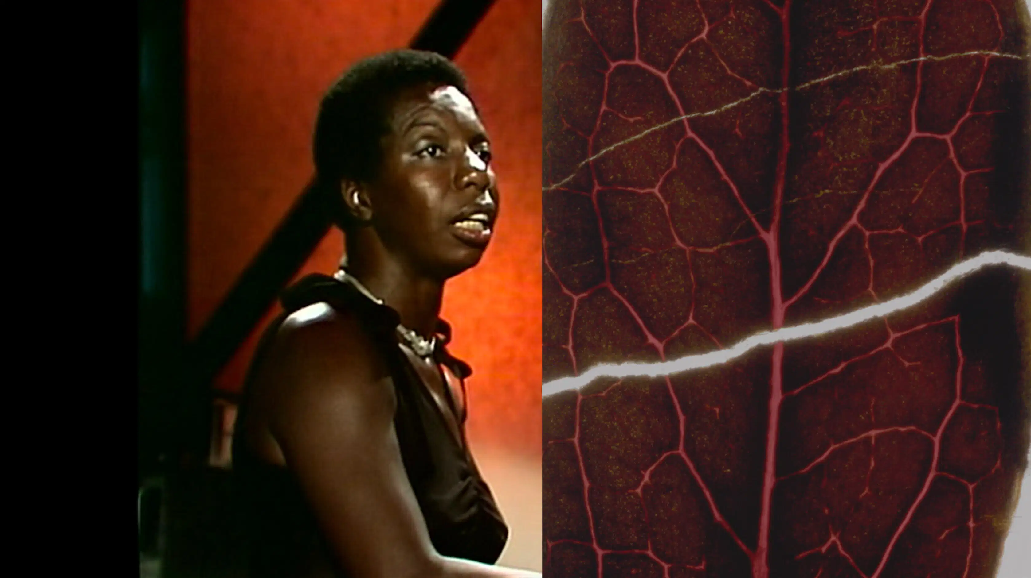 Video still of a woman looking off camera, sitting in an environment mostly composed of deep red tones. 