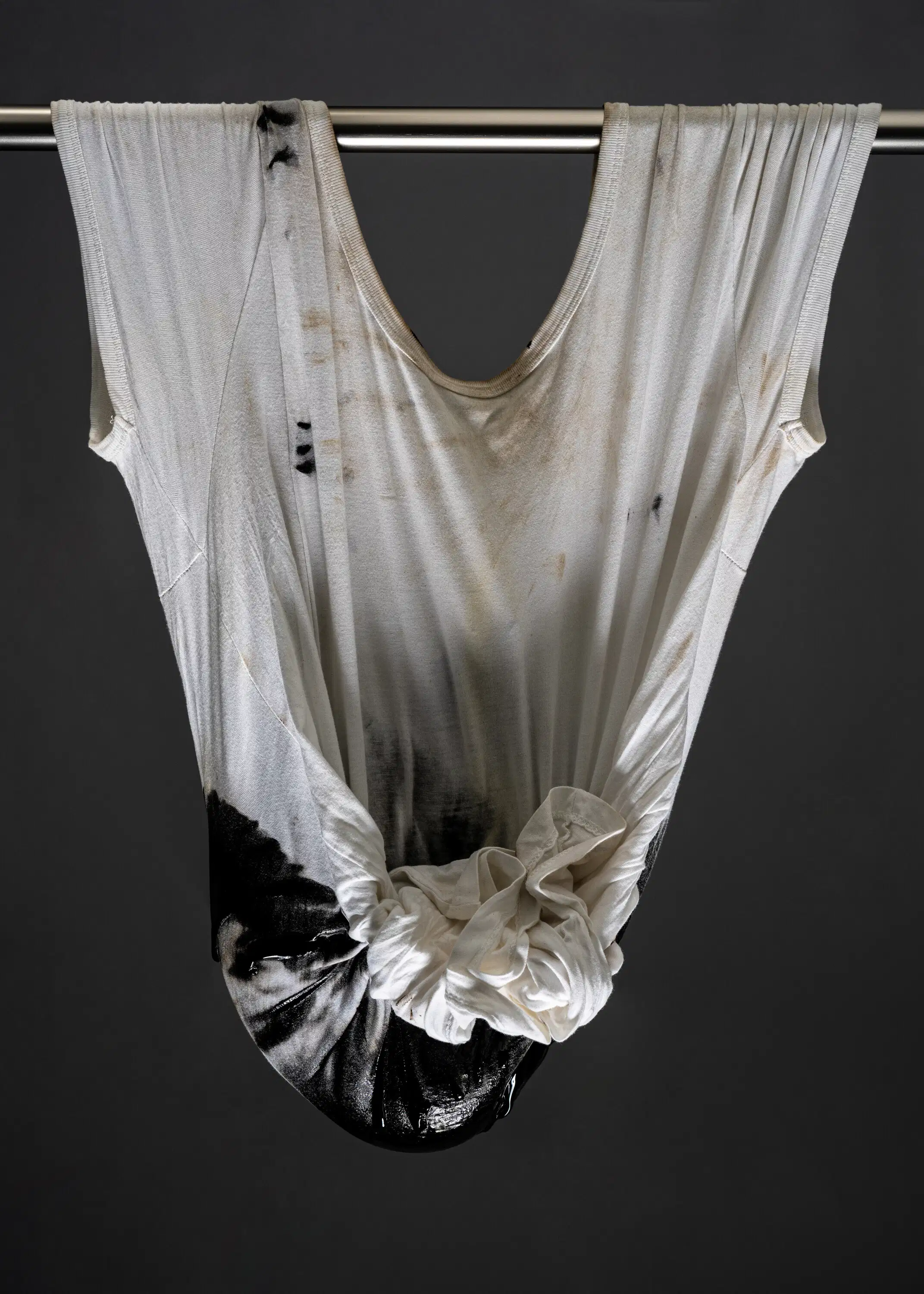 Still life photo of a dirtied white t-shirt hung by a curtain rod, which runs through the sleeve holes