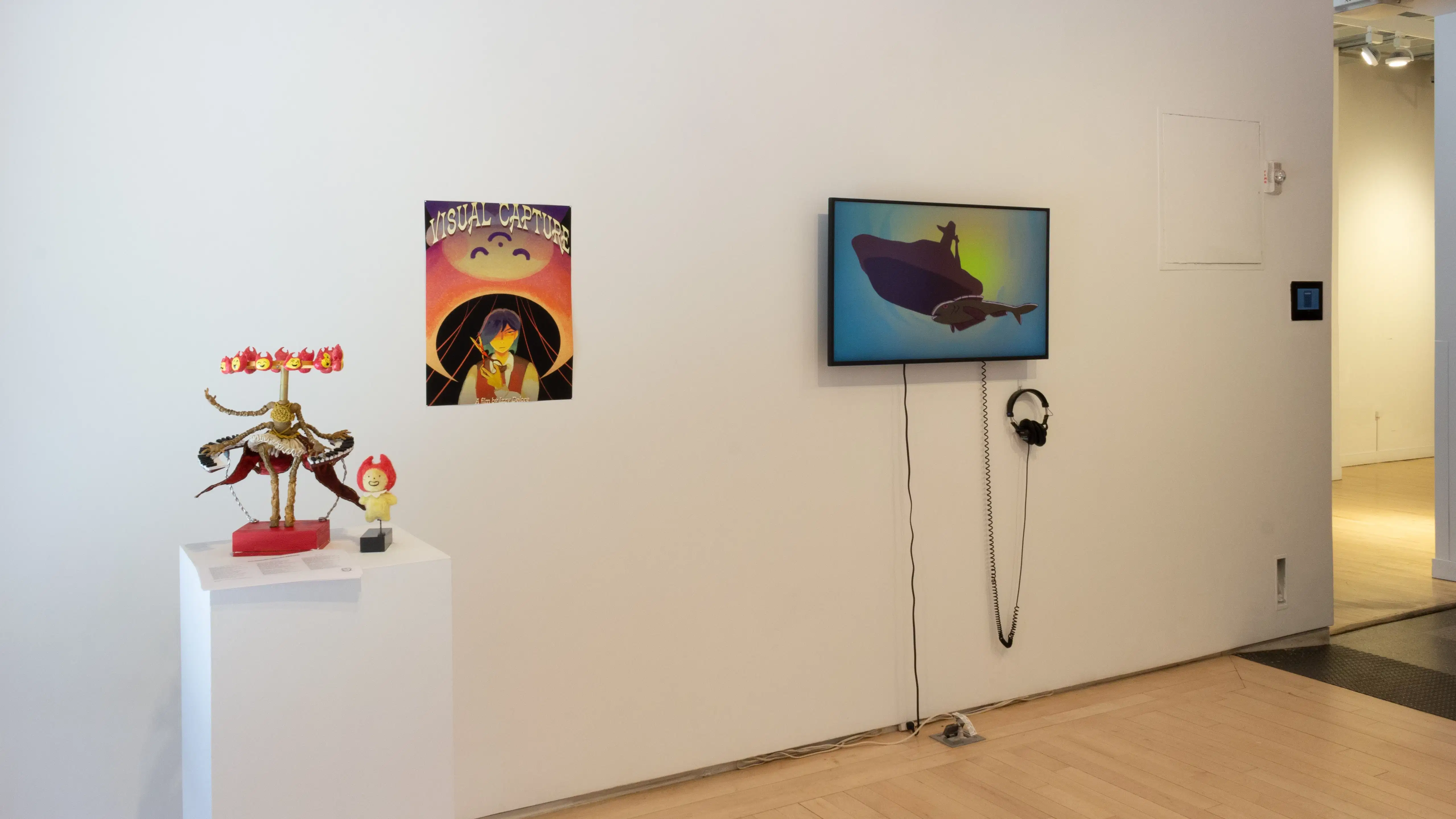 Installation image showing a monitor and a poster along a wall in a small room, with a pedestal with a sculpture on the floor.