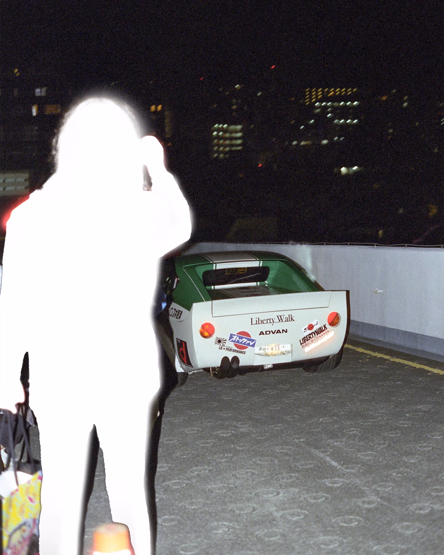 Colored photograph of a Datsun S30 Fairlady Z in Kaido Racer style driving away from the camera, with a figure in the left of the frame, digitally manipulated.