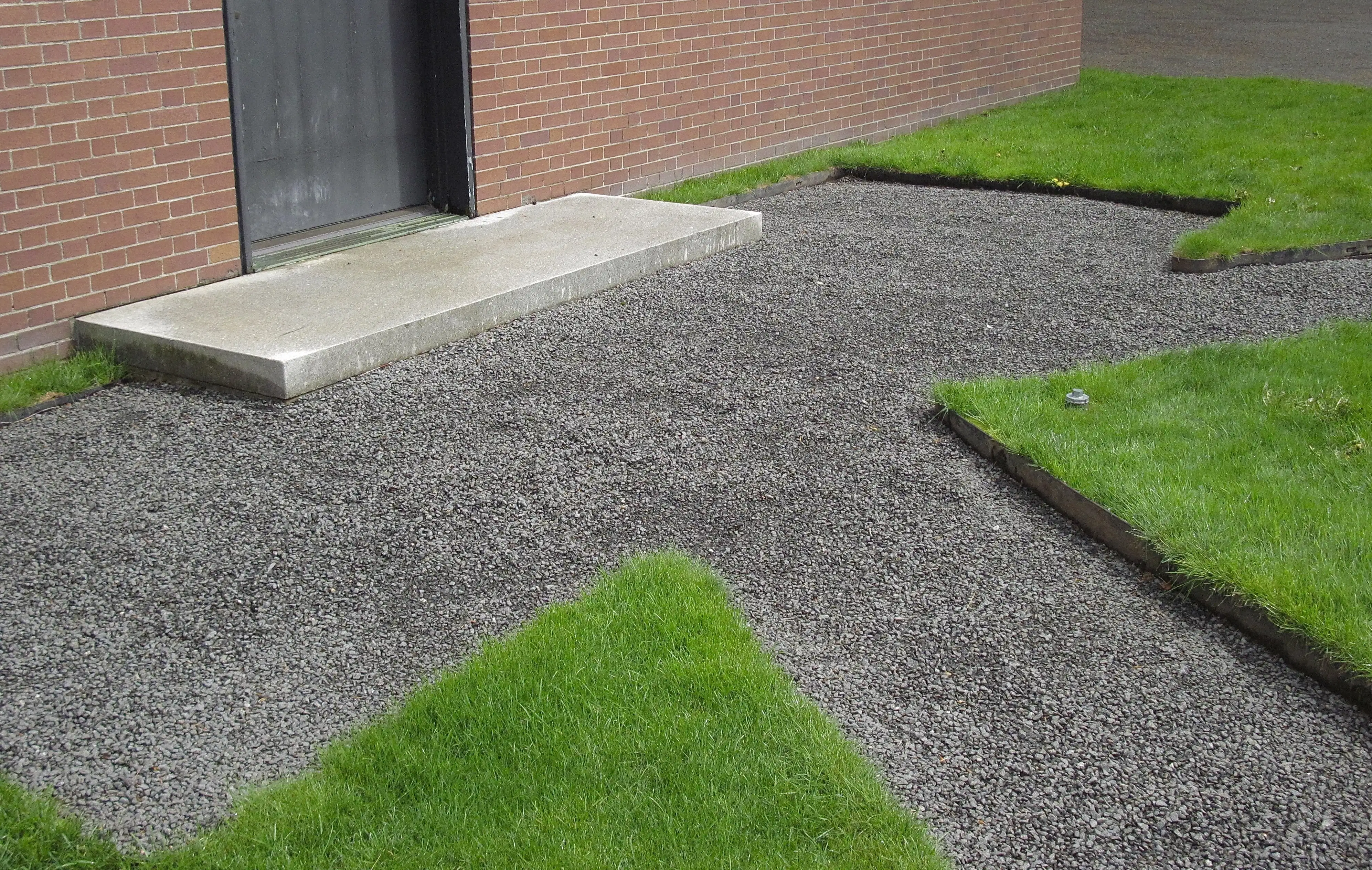 A gravel walkway leading to a door and surrounded by green grass.