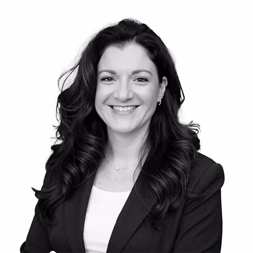A monochrome image cropped to below the shoulders of a woman with dark brown hair, a white shirt, and black blazer.