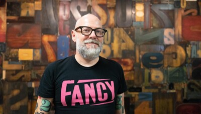 Faculty member Dan Rhatigan wearing black glasses and a pink and black t-shirt that says "Fancy" in typeface.
