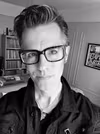 Faculty member Joe Newton wearing black rimmed glasses and a black shirt.