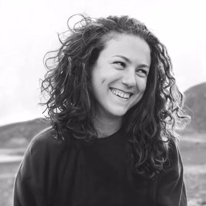 A black and white portrait of a woman smiling with curly hair with mountains in the background.