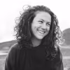 A black and white portrait of a woman smiling with curly hair with mountains in the background.