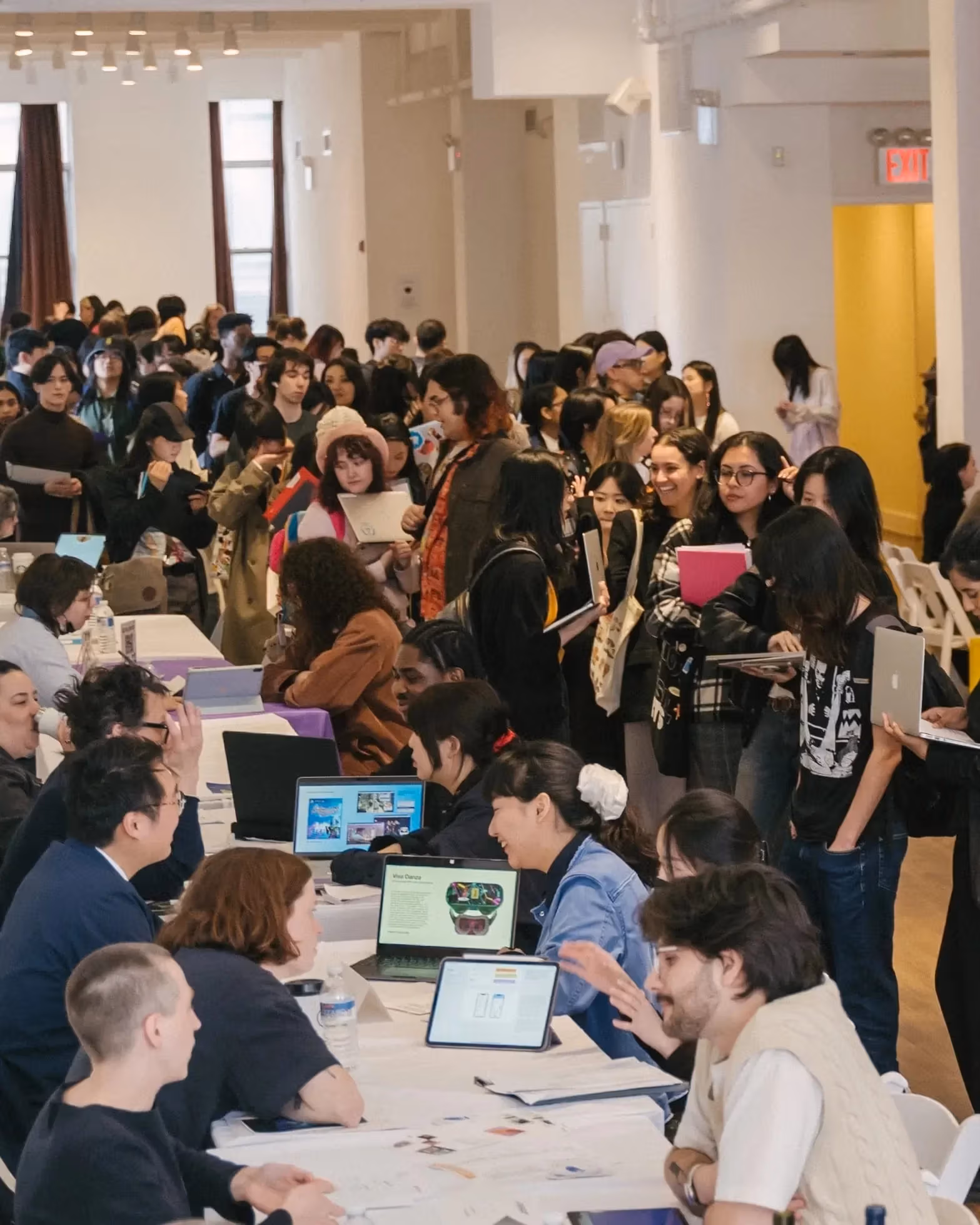 A highly attended career fair event in a large room wherein students mill about from table to table talking to prospective employers