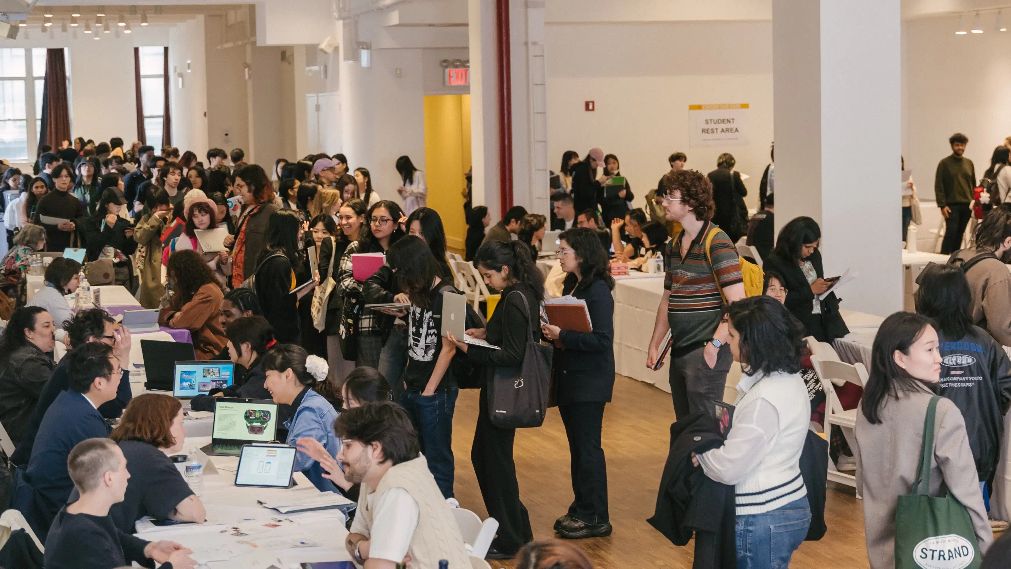 A highly attended career fair event in a large room wherein students mill about from table to table talking to prospective employers