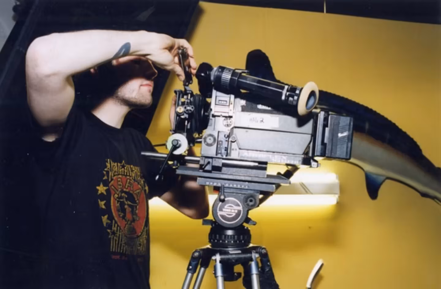 Person in a graphic t-shirt operating a video camera on a tripod