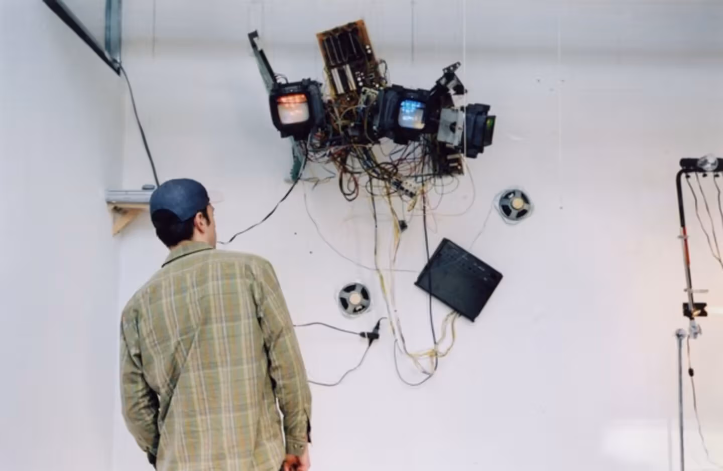 Person with back to the camera in the foreground; behind them, a mixed media assemblage suspended from the ceiling
