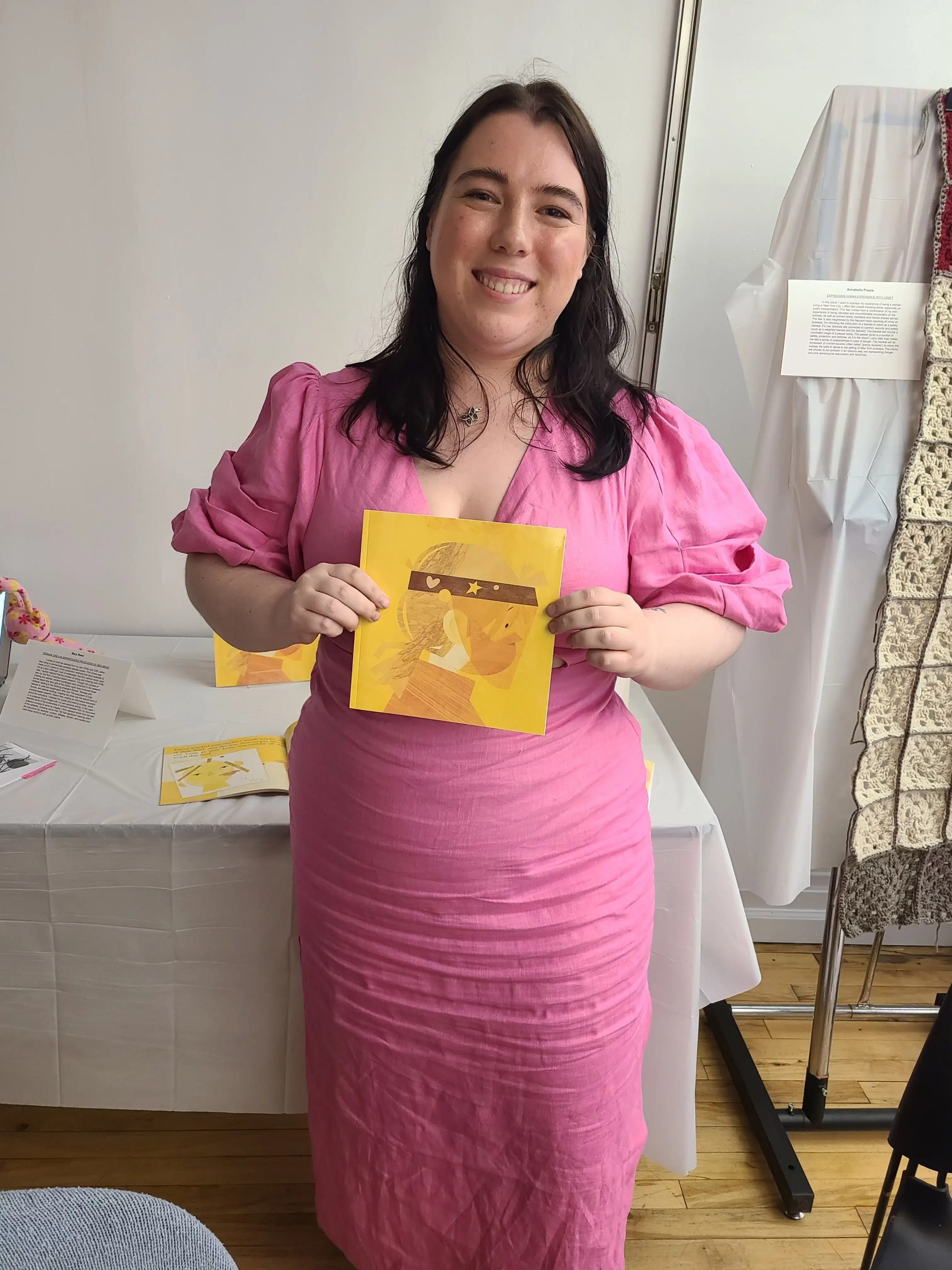 Person in a pink dress holds a children's book depicting a person with a face mask and protective shield on.