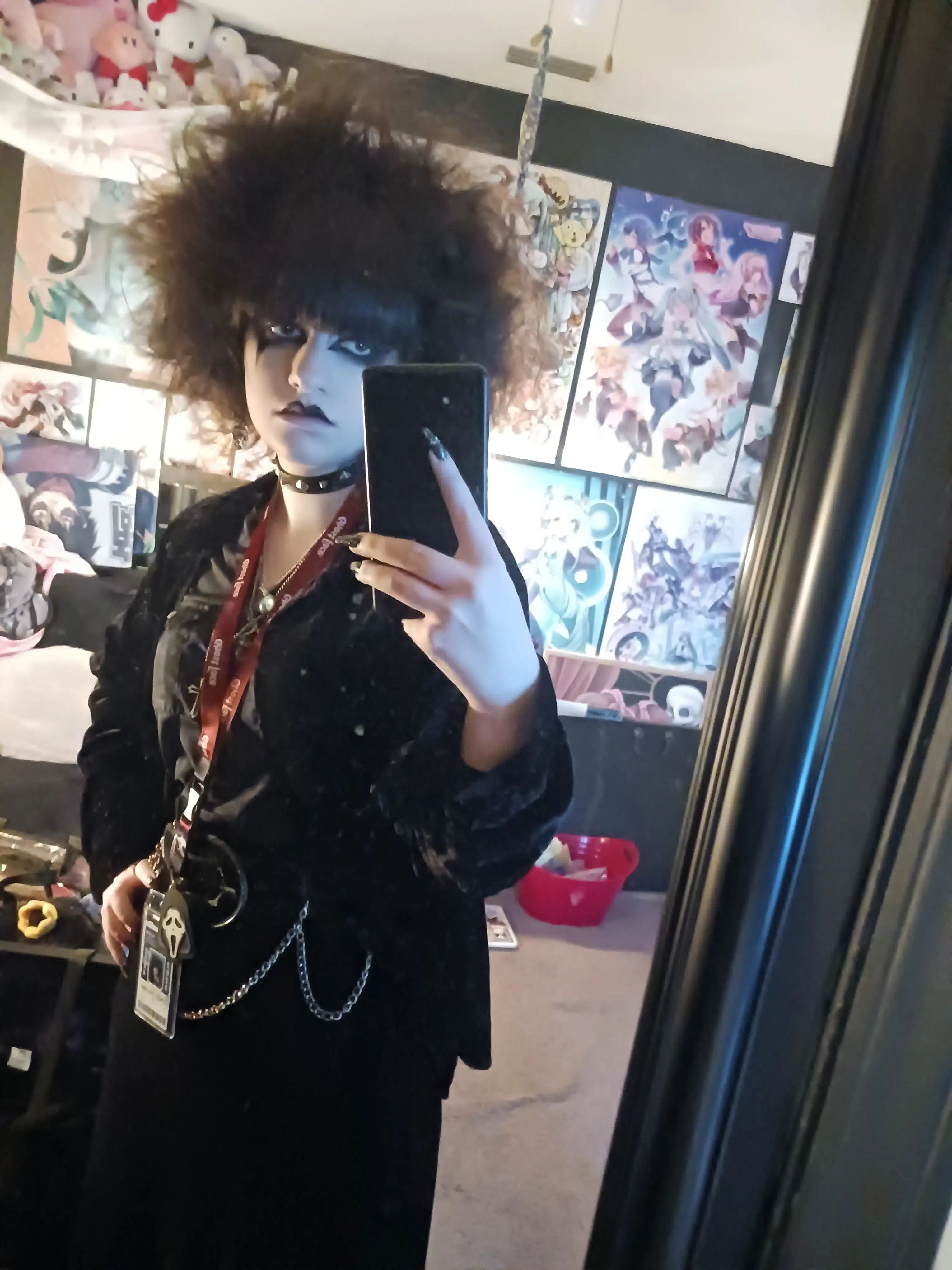 An individual dressed in alternative, punk/goth clothing takes a mirror selfie.