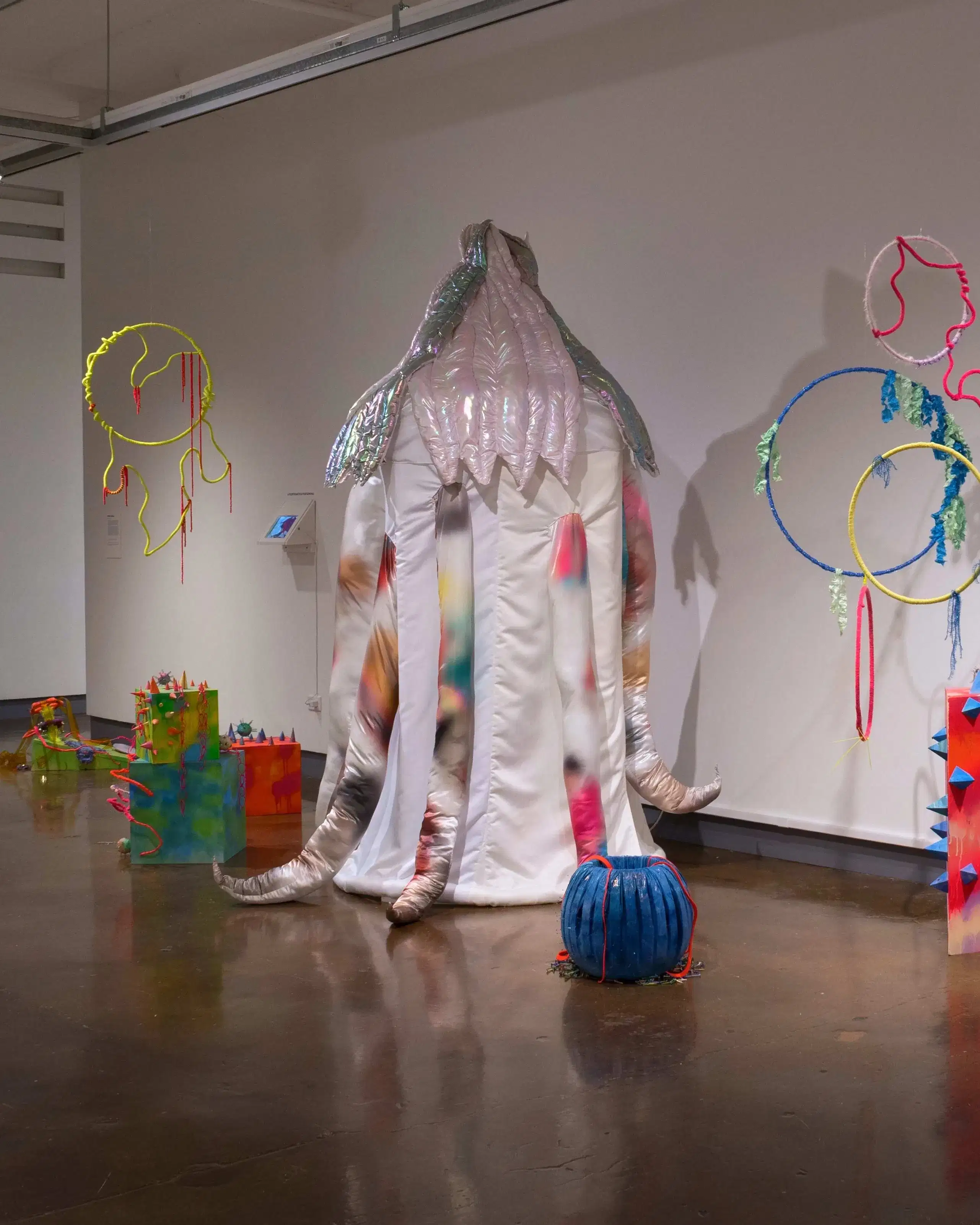 Multiple abstract sculptures are placed on the floor or hang from the ceiling. They're made up of a lot of loopy shapes and bright colors.