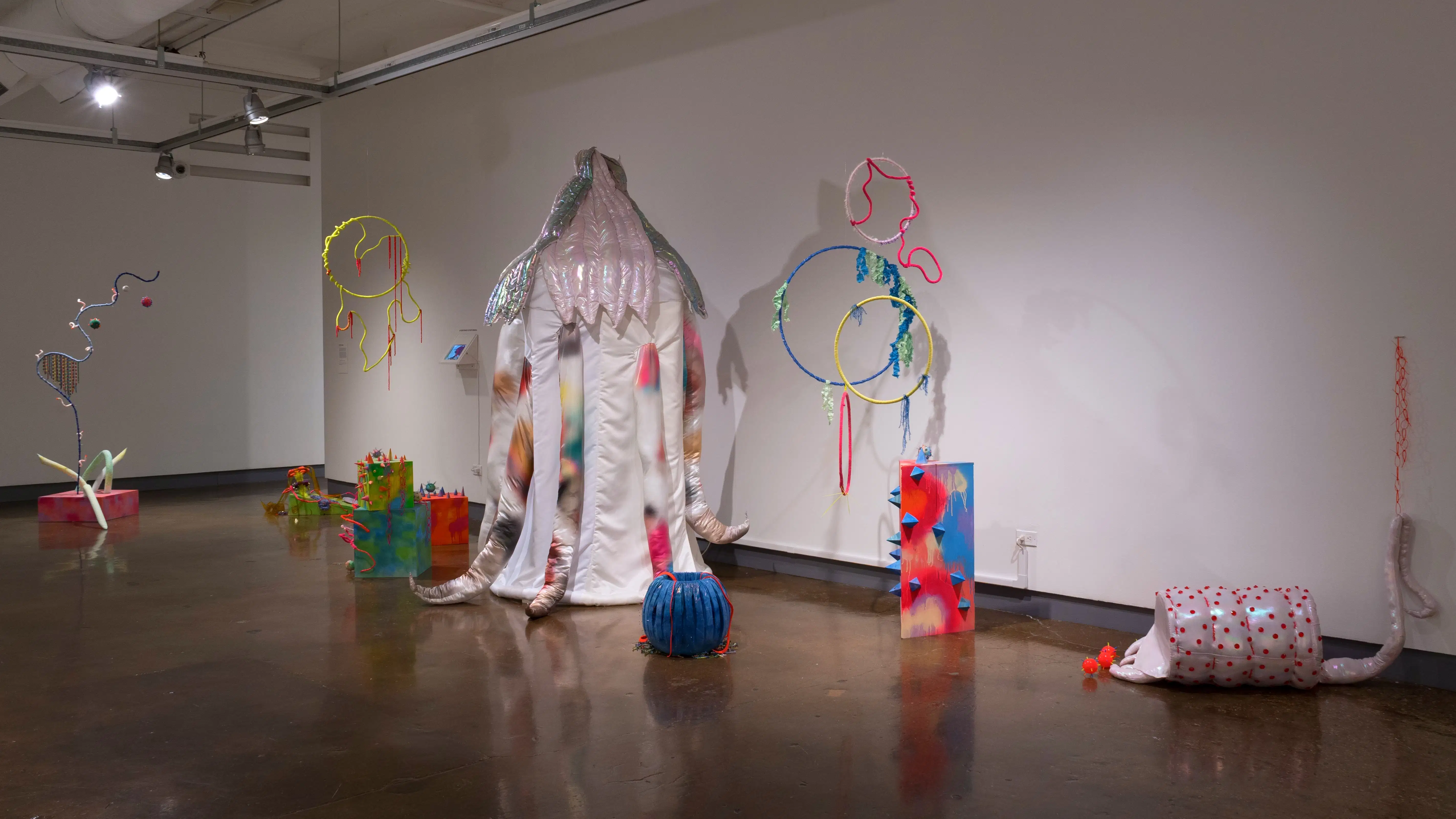 Multiple abstract sculptures are placed on the floor or hang from the ceiling. They're made up of a lot of loopy shapes and bright colors.