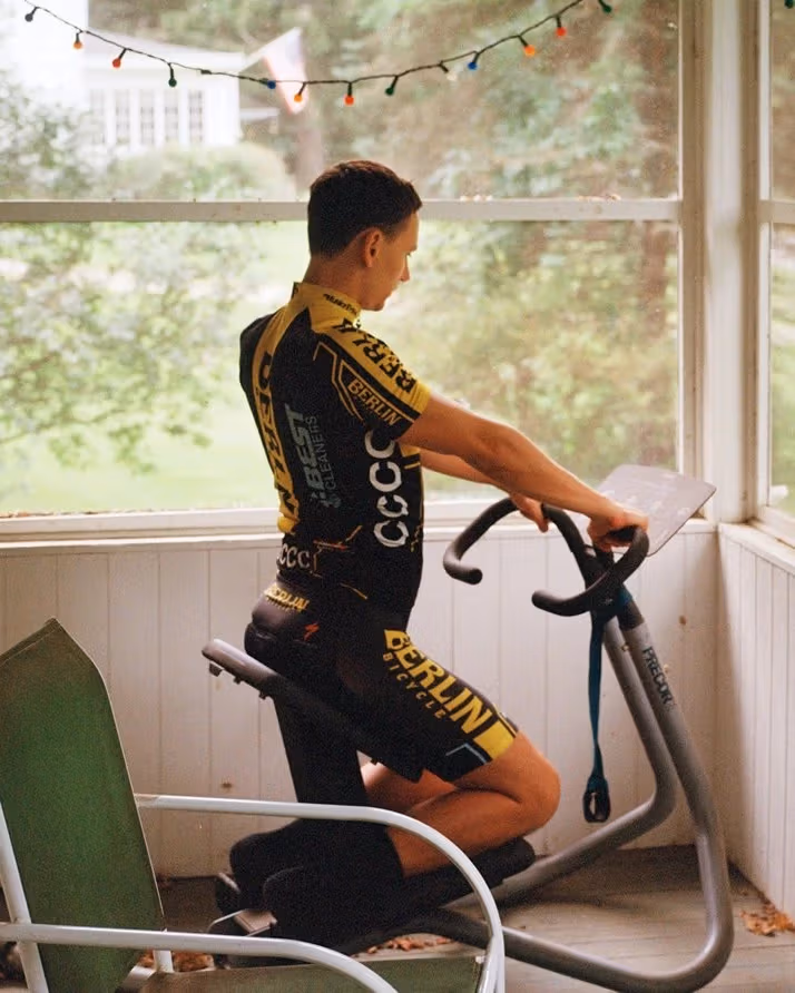 Photograph of a light-skinned man on exercise bike looking at a list of movements while inside an enclosed patio or sunroom.
