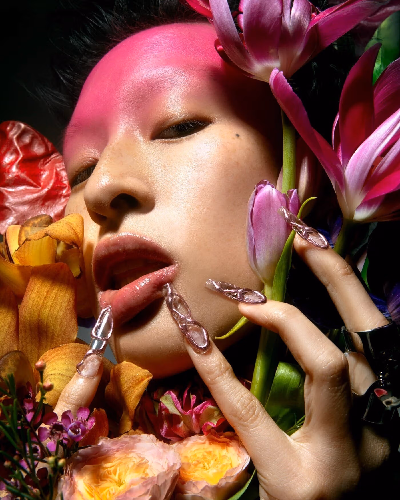 Close up portrait of a person with long nails holding several flowers close to their face.