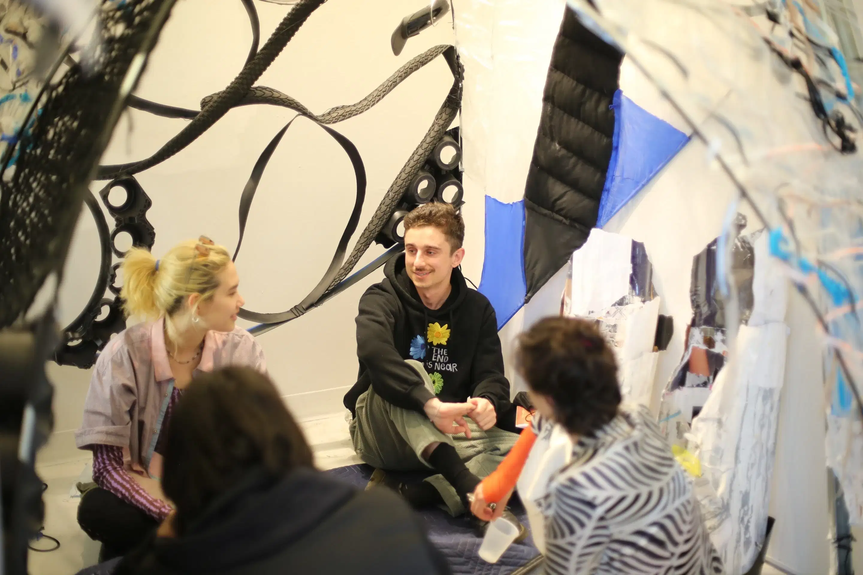 Four people sitting cross-legged on the floor inside of a sculpture and chatting. 