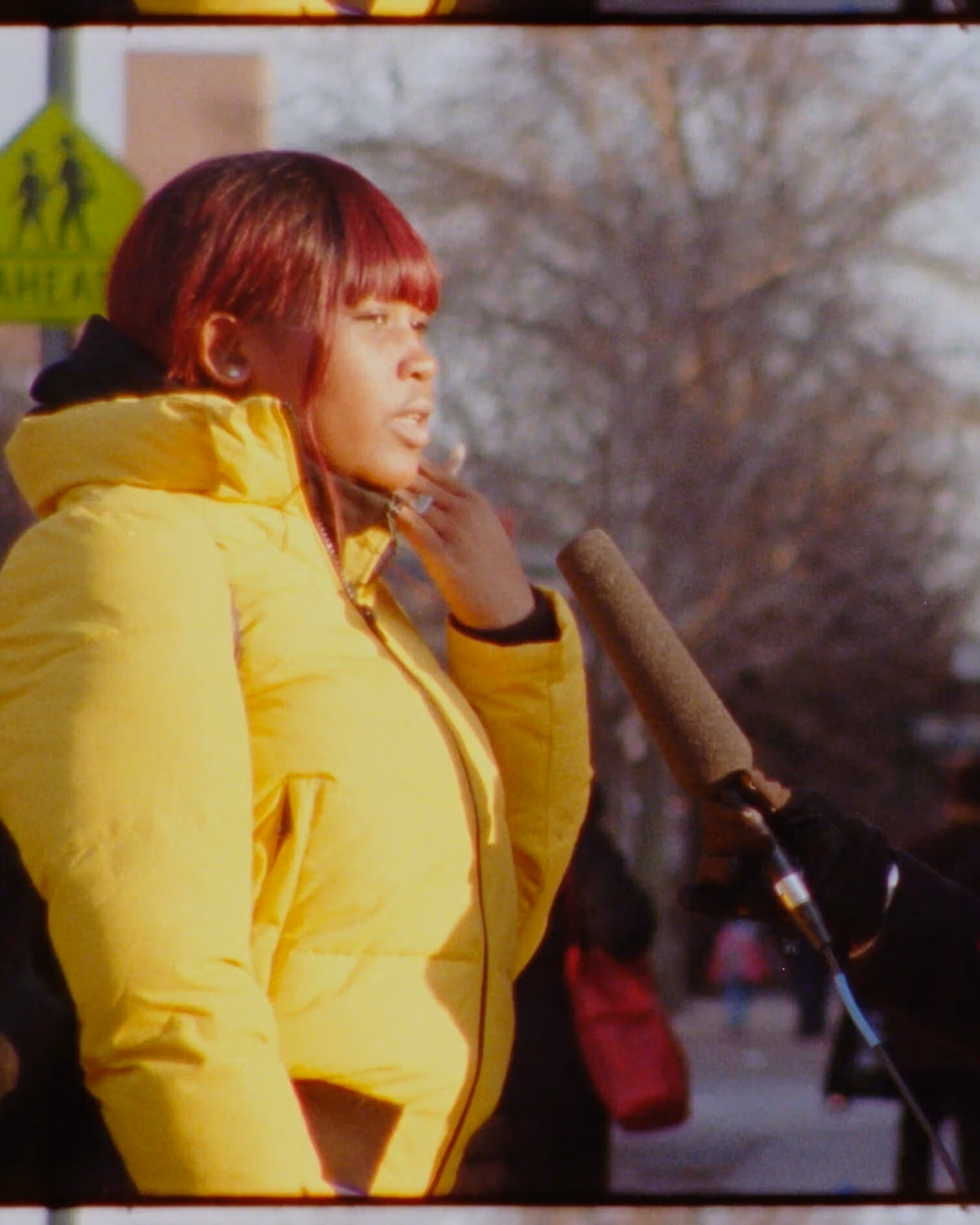 Video still of a woman interviewing another woman on the street. The interviewer hold a large microphone up. 
