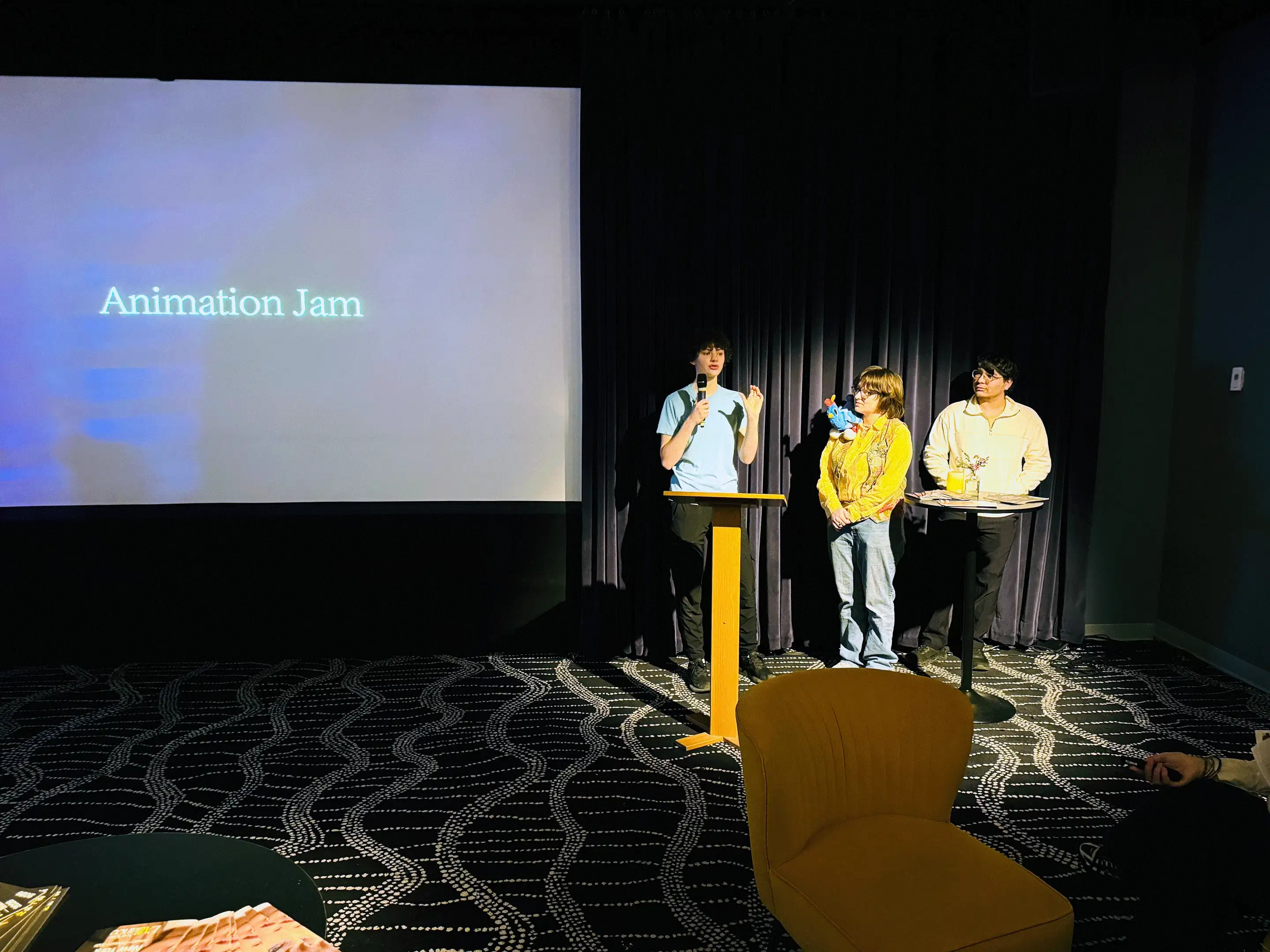 Three individuals stand onstage next to a large projection screen that reads “Animation Jam.”