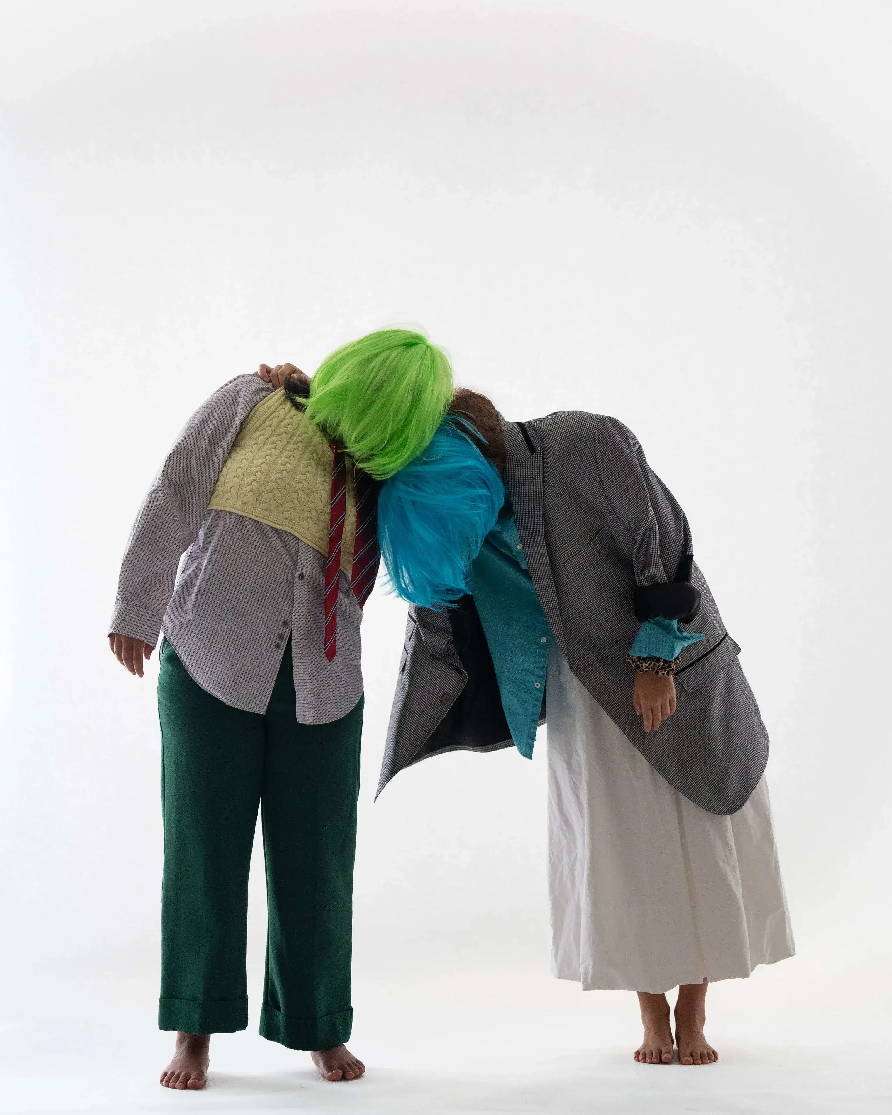 Two people in wigs with obscured faces lean on each other.