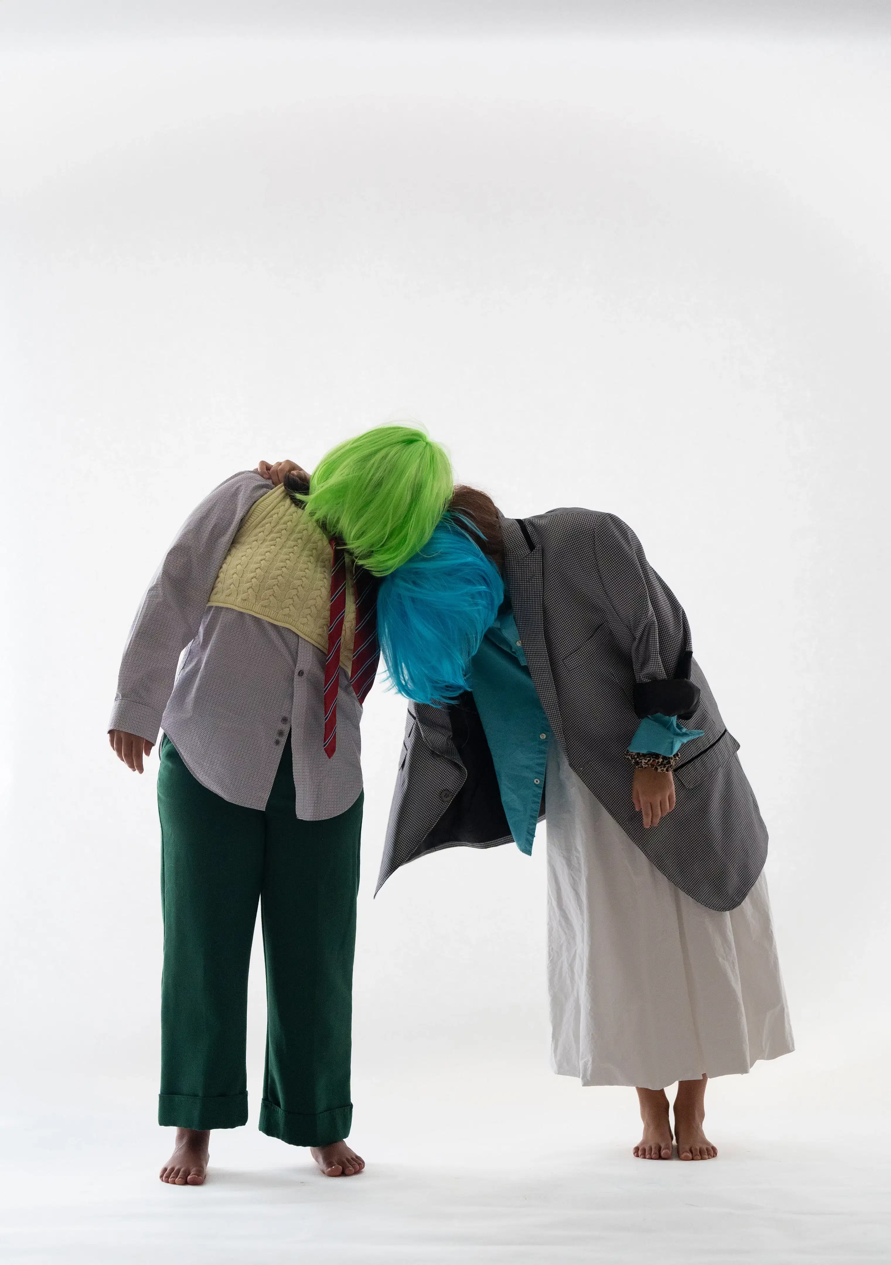 Two people in wigs with obscured faces lean on each other.