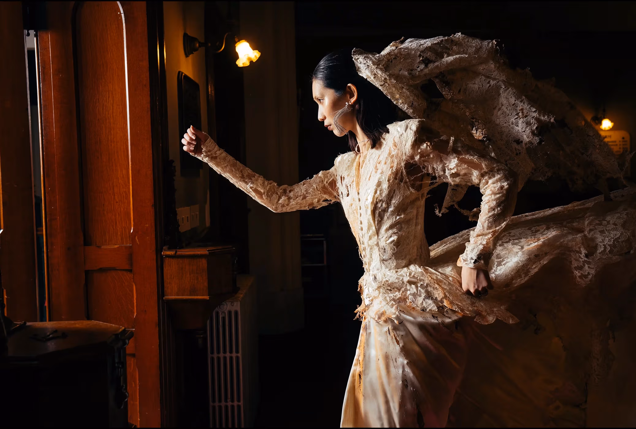 A woman in a burnt wedding dress runs out of a dimly lit building towards the door where light is coming through