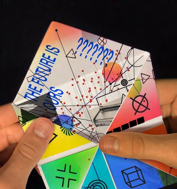 A photograph of hands holding a white paper chatterbox, aka, a "paper fortune teller."