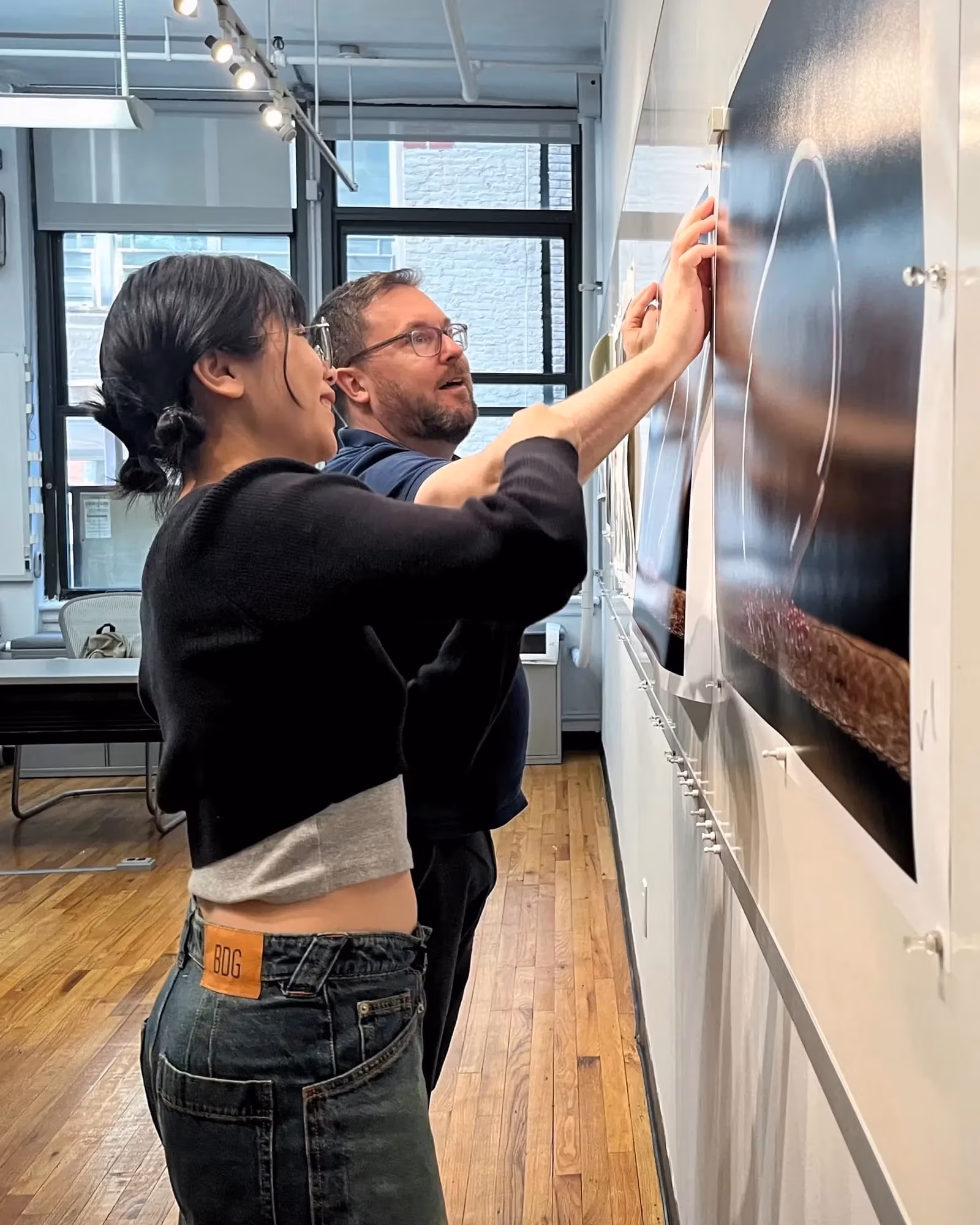 a student and professor examine a photo print that hangs on a wall.