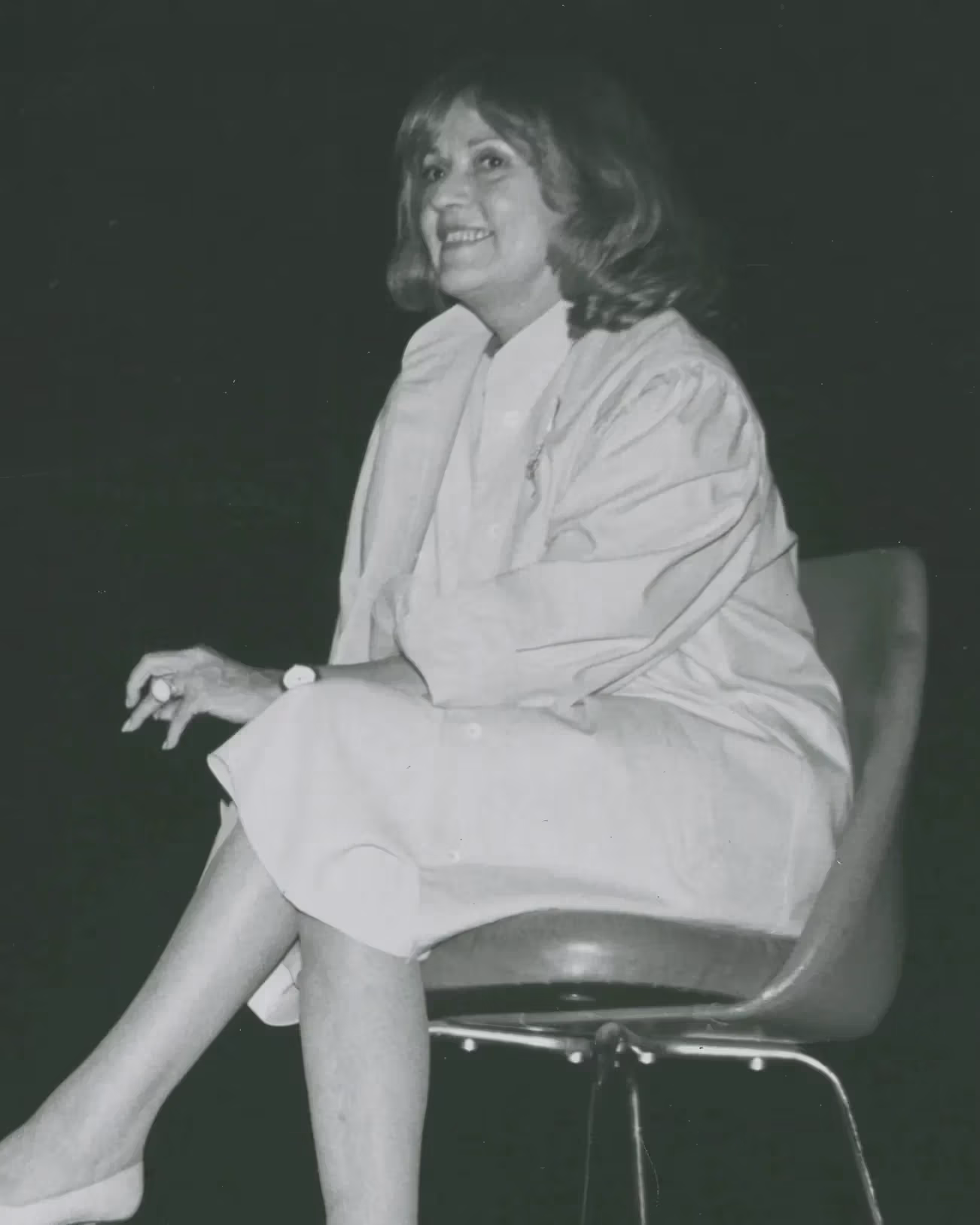 Two people sit in chairs on a stage in mid-discussion. The person on the left is pointing to something off-camera and both people are smiling.