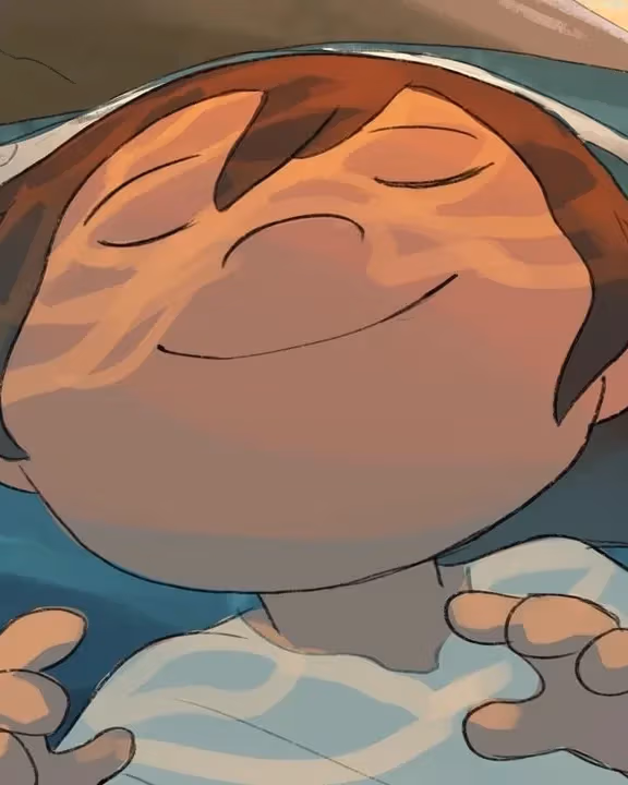 A boy smiles as water washes over him, the orange light from the setting sun illuminating his face.