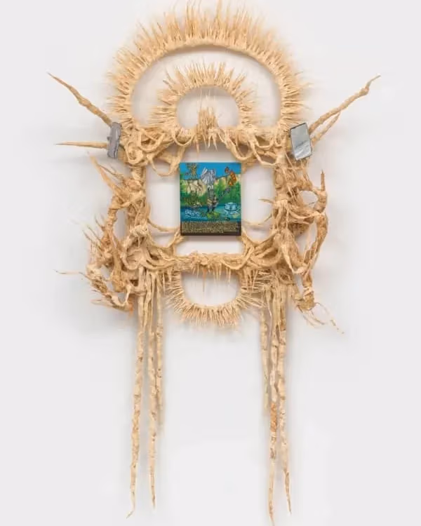 A small oil painting framed by a sculpture reminiscent of a headdress.