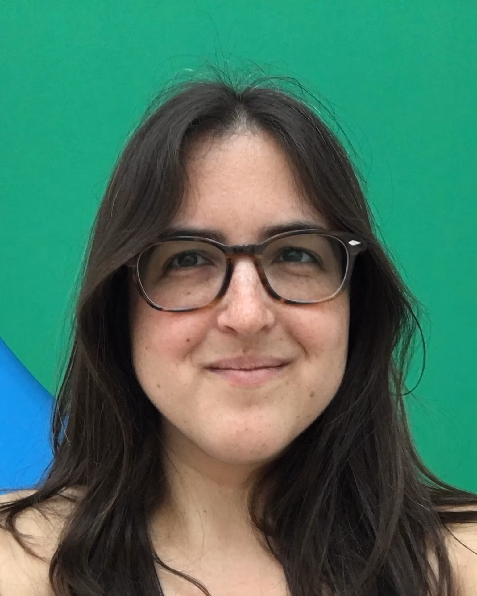 Curator Hayley Ferber smiles at the camera wearing glasses and standing in front of an abstract green and blue background.