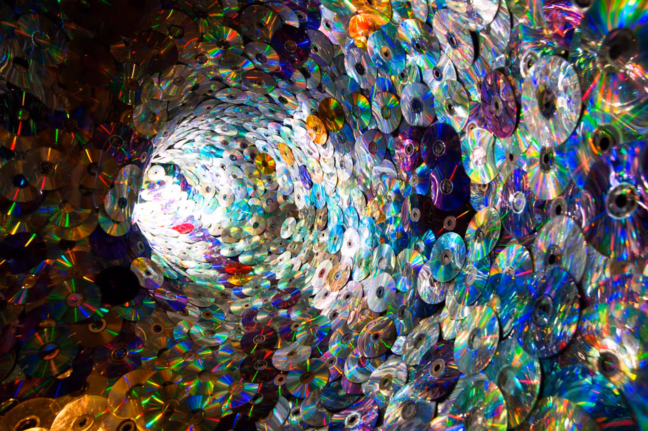 A tunnel made up of iridescent plastic CDs. A light is visible at the end of the tunnel.