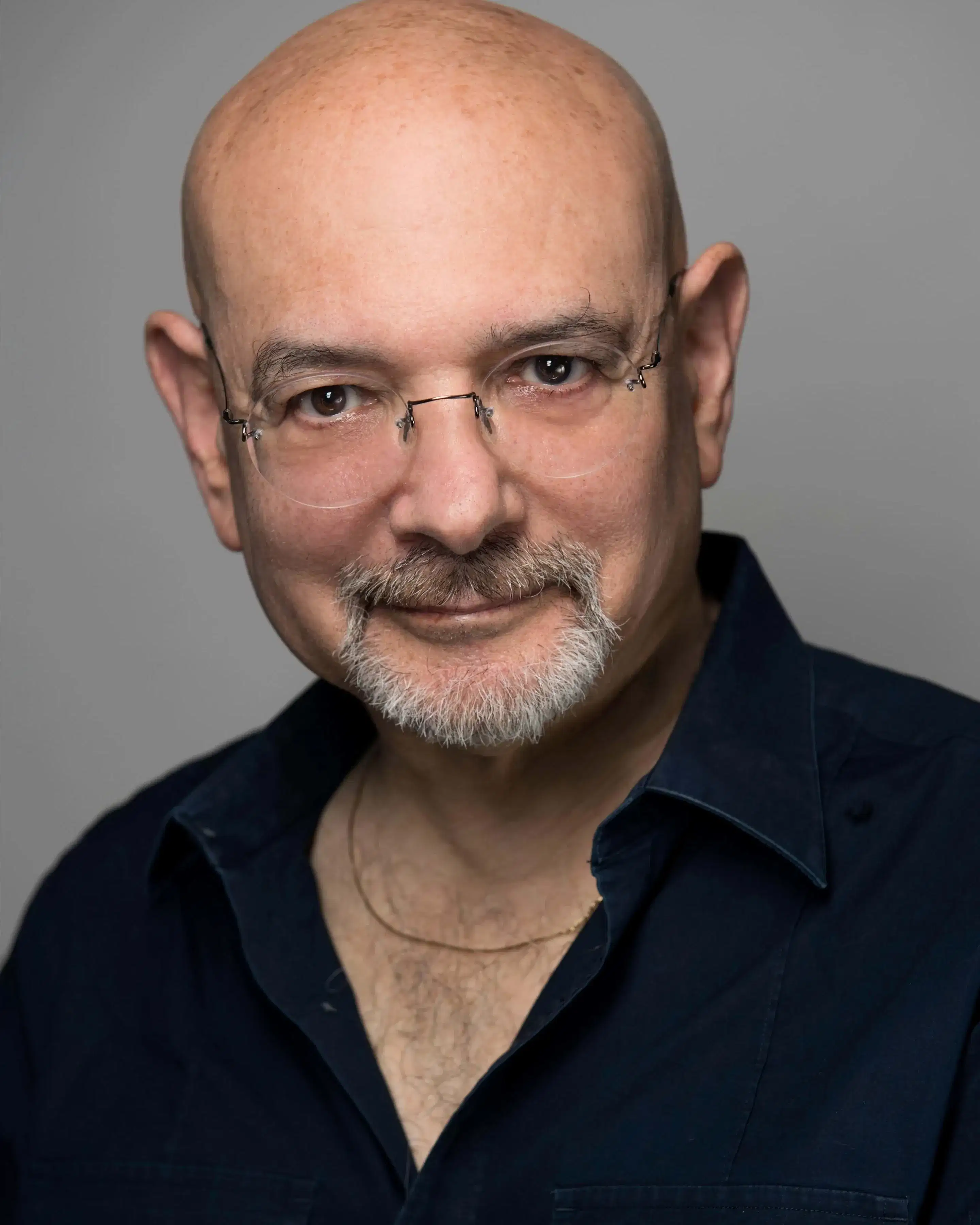 A white man with glasses and a goatee, wearing a dark shirt, poses against a plain background.